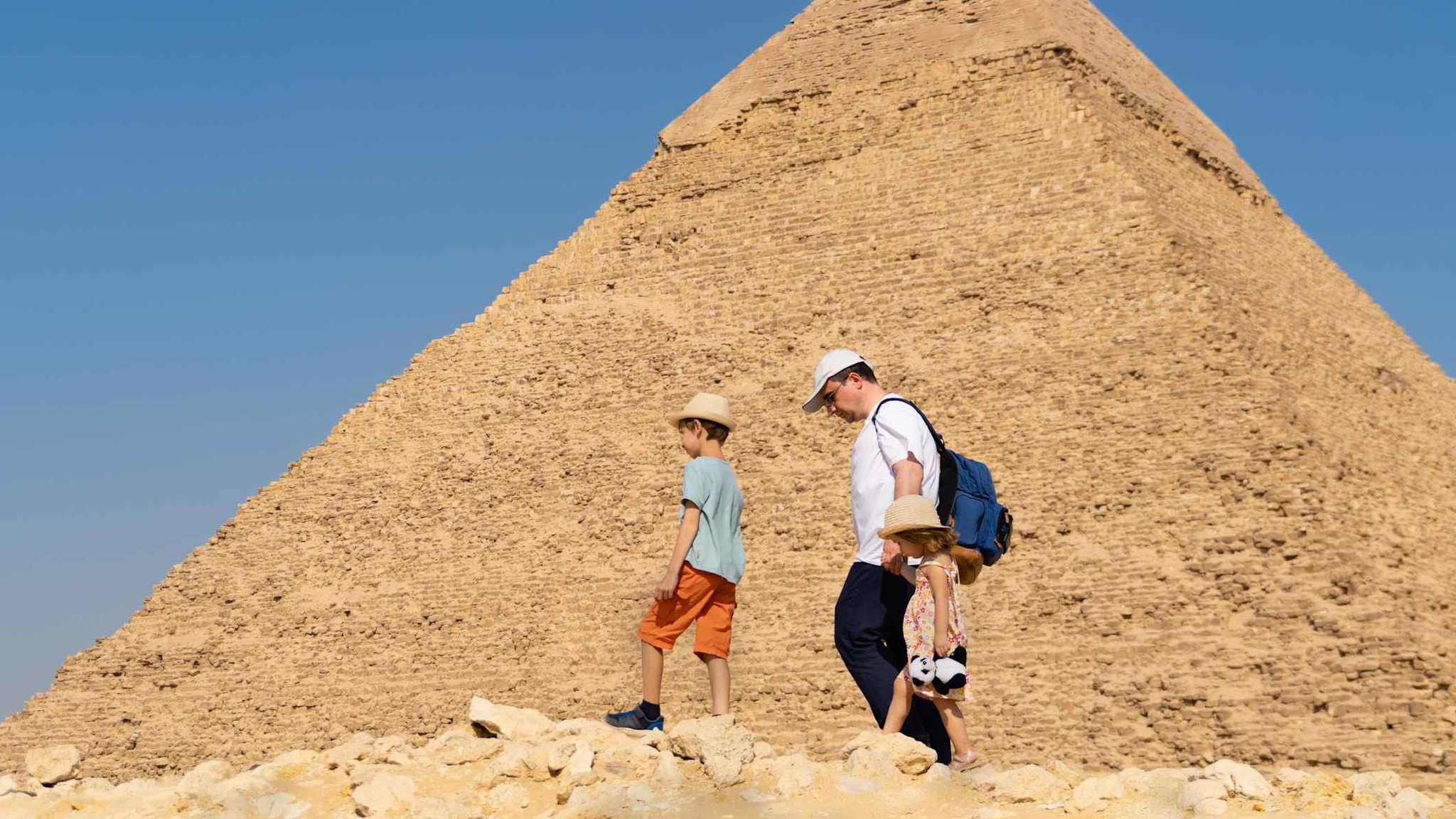 Ein Vater läuft mit seinen Kindern an einer Pyramide von Gizeh, Ägypten, entlang.