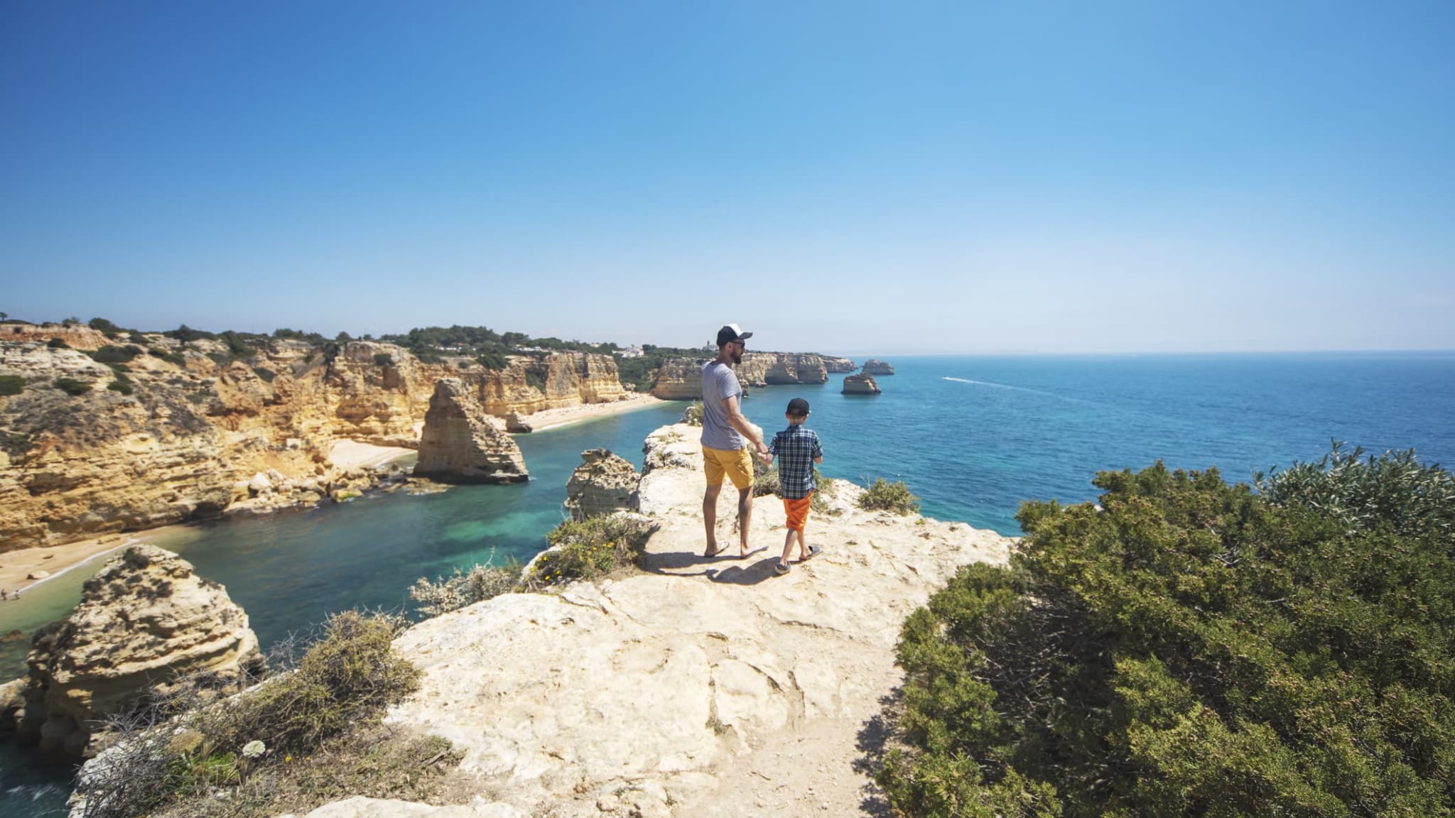 Vater und Sohn spazieren an einer Klippe entlang in der Algarve, Portugal.
