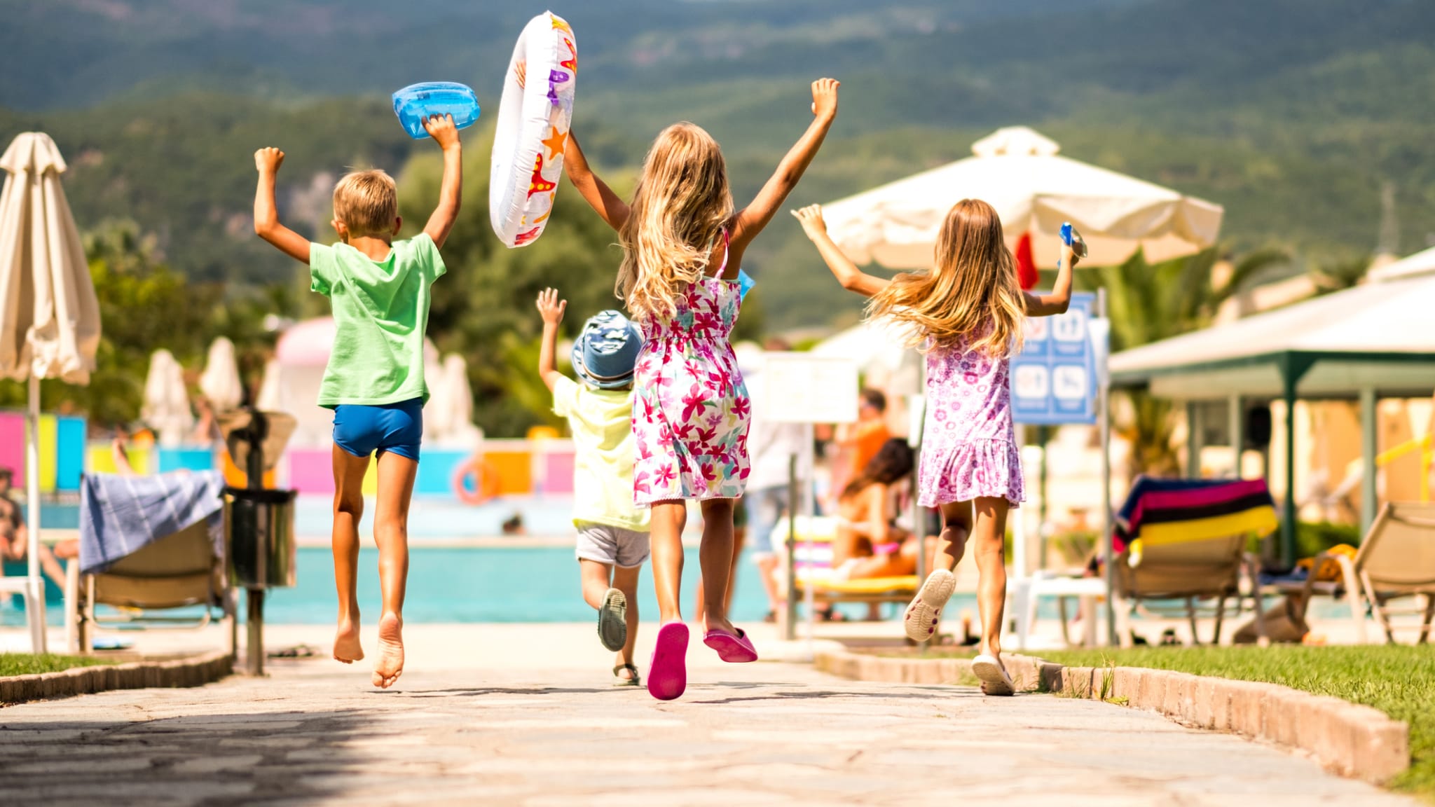 Vier Kinder rennen voller Vorfreude zu einem Pool.