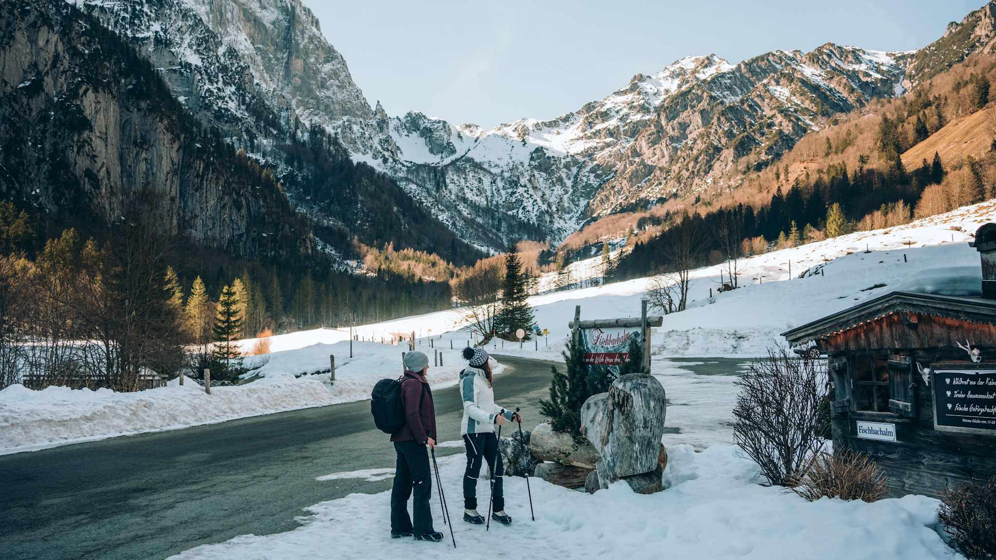 Zwei Frauen wandern an einer Hütte in den Bergen vorbei.