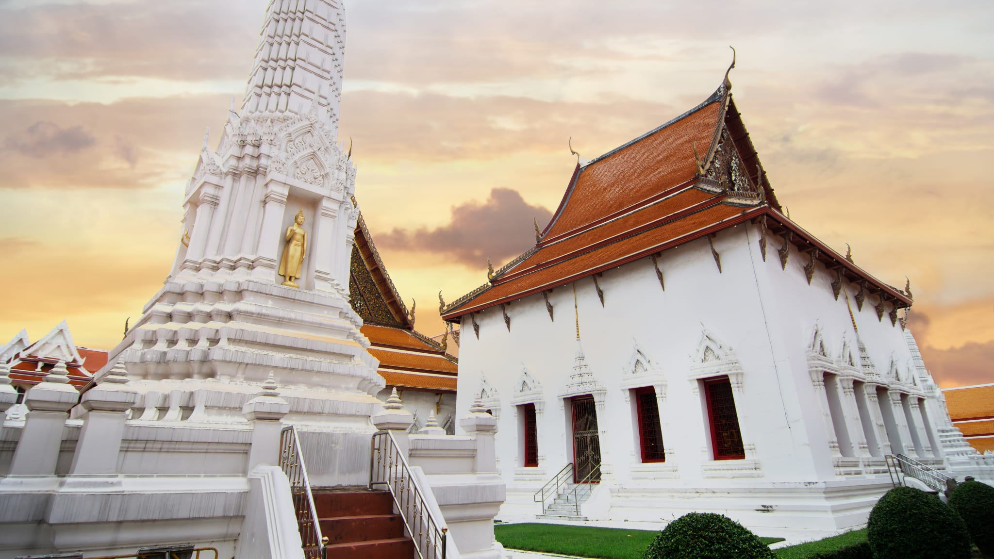 Neben einer Stupa mit Buddhastatue steht ein quadratisch angelegtes Tempelgebäude.