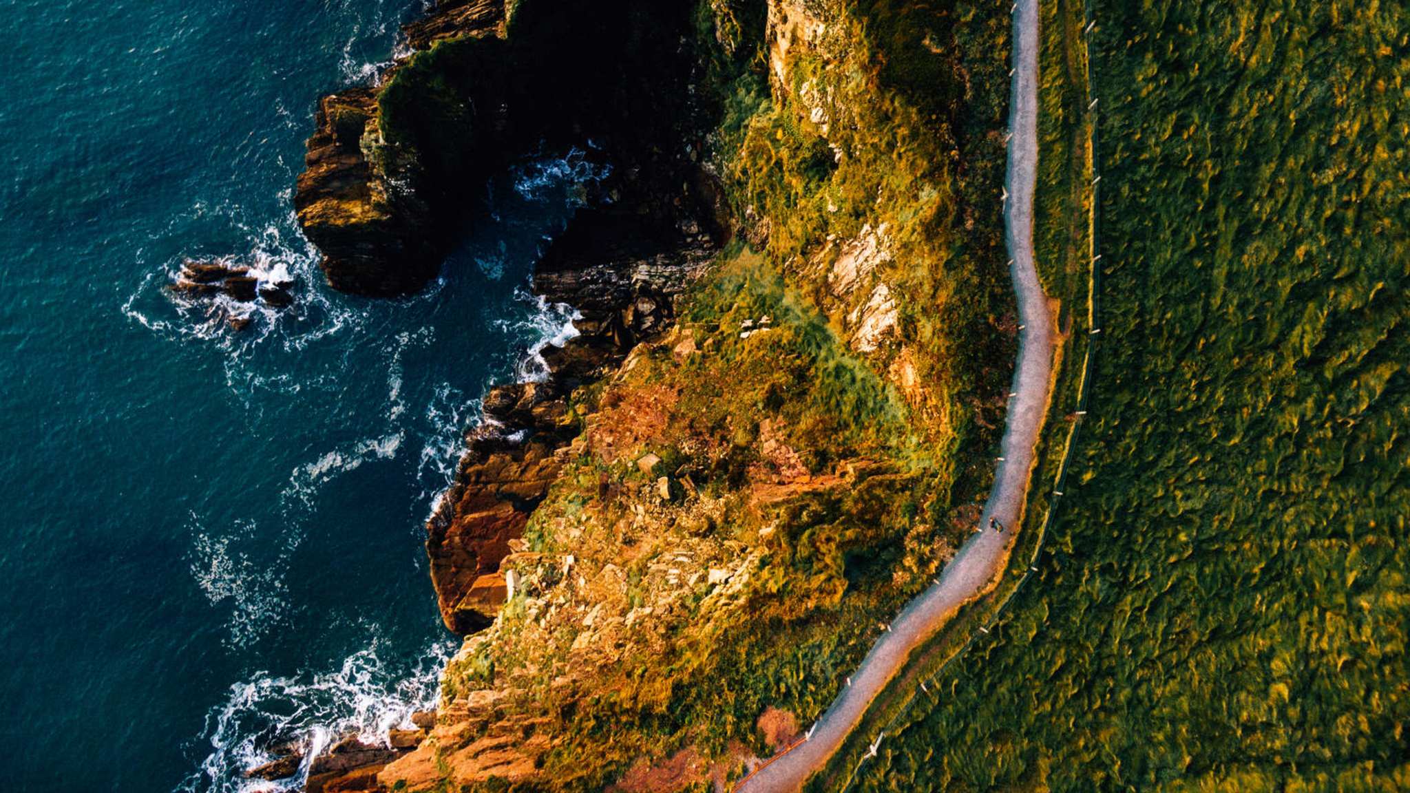 Luftaufnahme einer Küstenstraße, die an Feldern und Klippen vorbei führt.