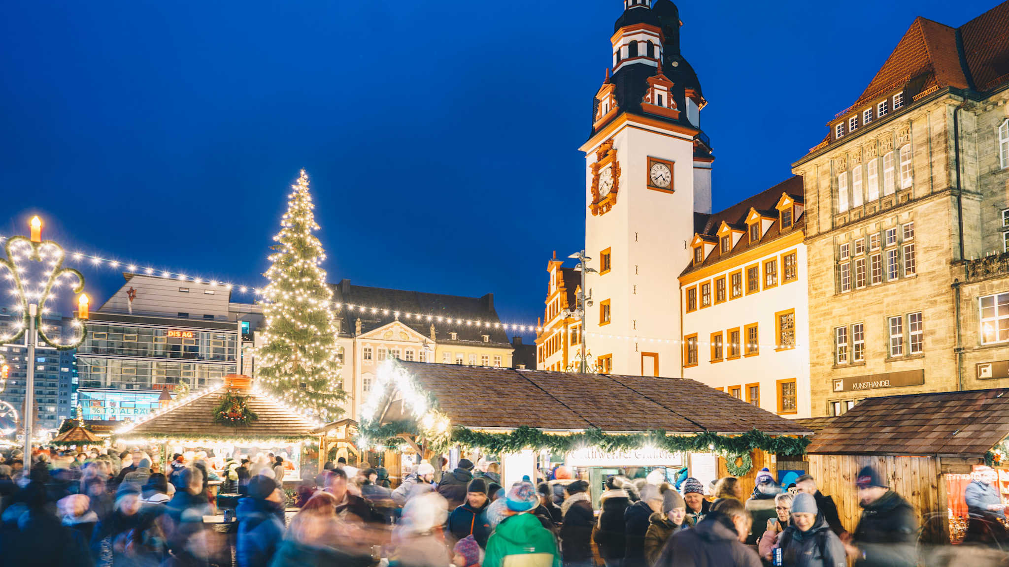 Menschen gehen über einen Weihnachtsmarkt vor einem große Turm.