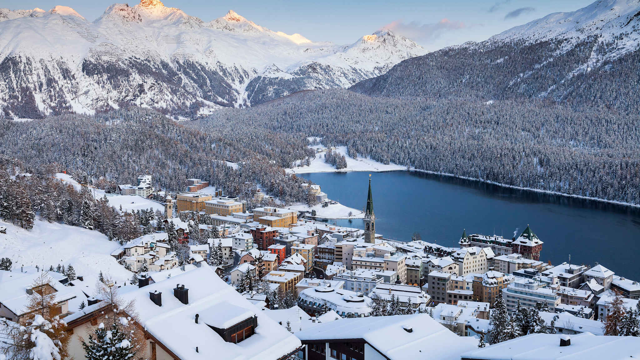 Eine verschneite Stadt an einem See in den Bergen.