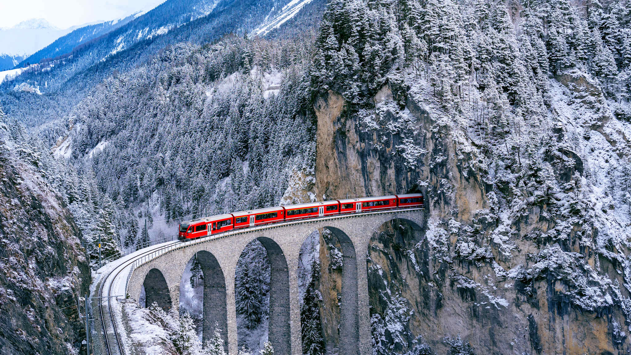Ein Zug fährt über eine Brücke in einem winterlichen Tal.