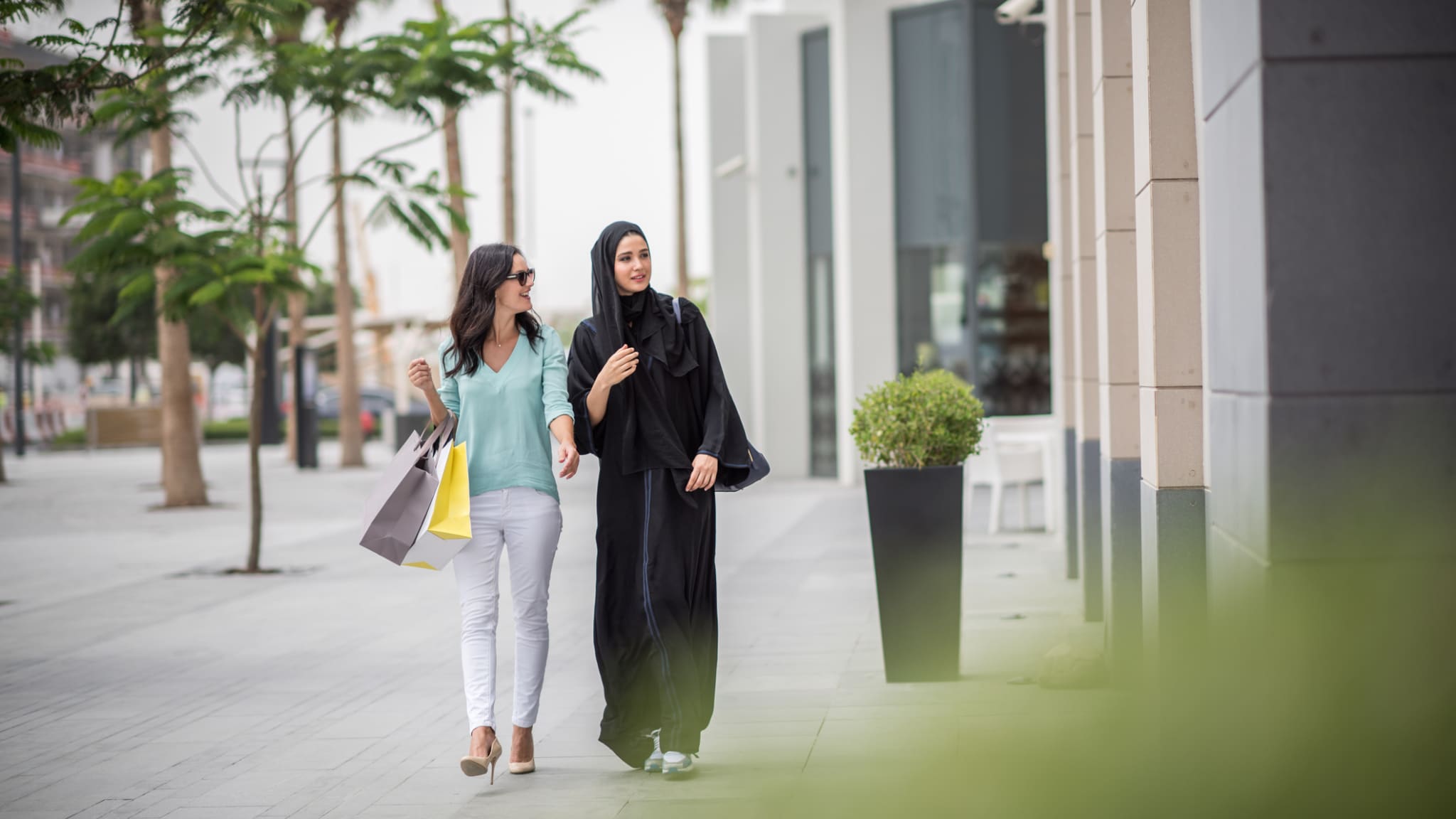 Zwei Frauen laufen gemeinsam durch Dubai mit Einkaufstüten.