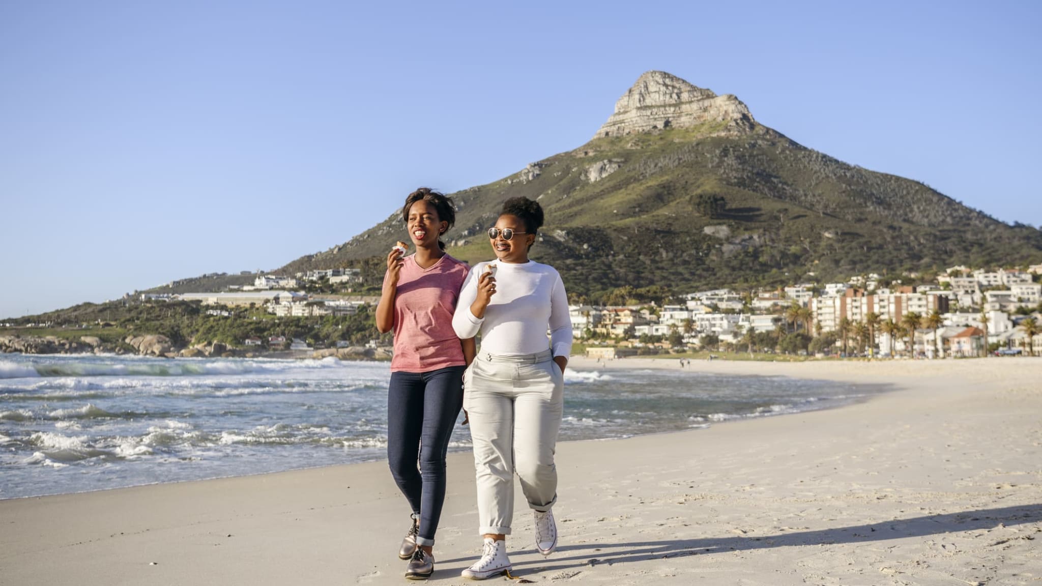 Zwei junge Frauen essen gemeinsam am Strand Eis.
