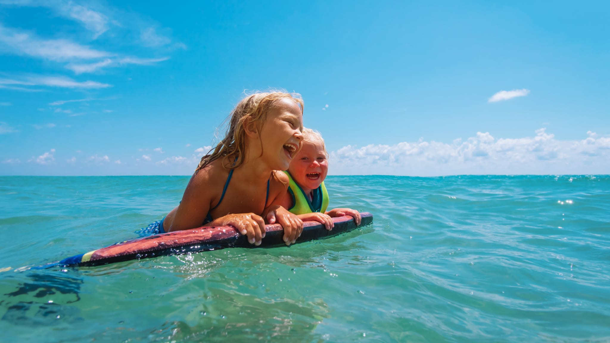 Zwei Kinder schwimmen mit einem Schwimmbrett im Meer.