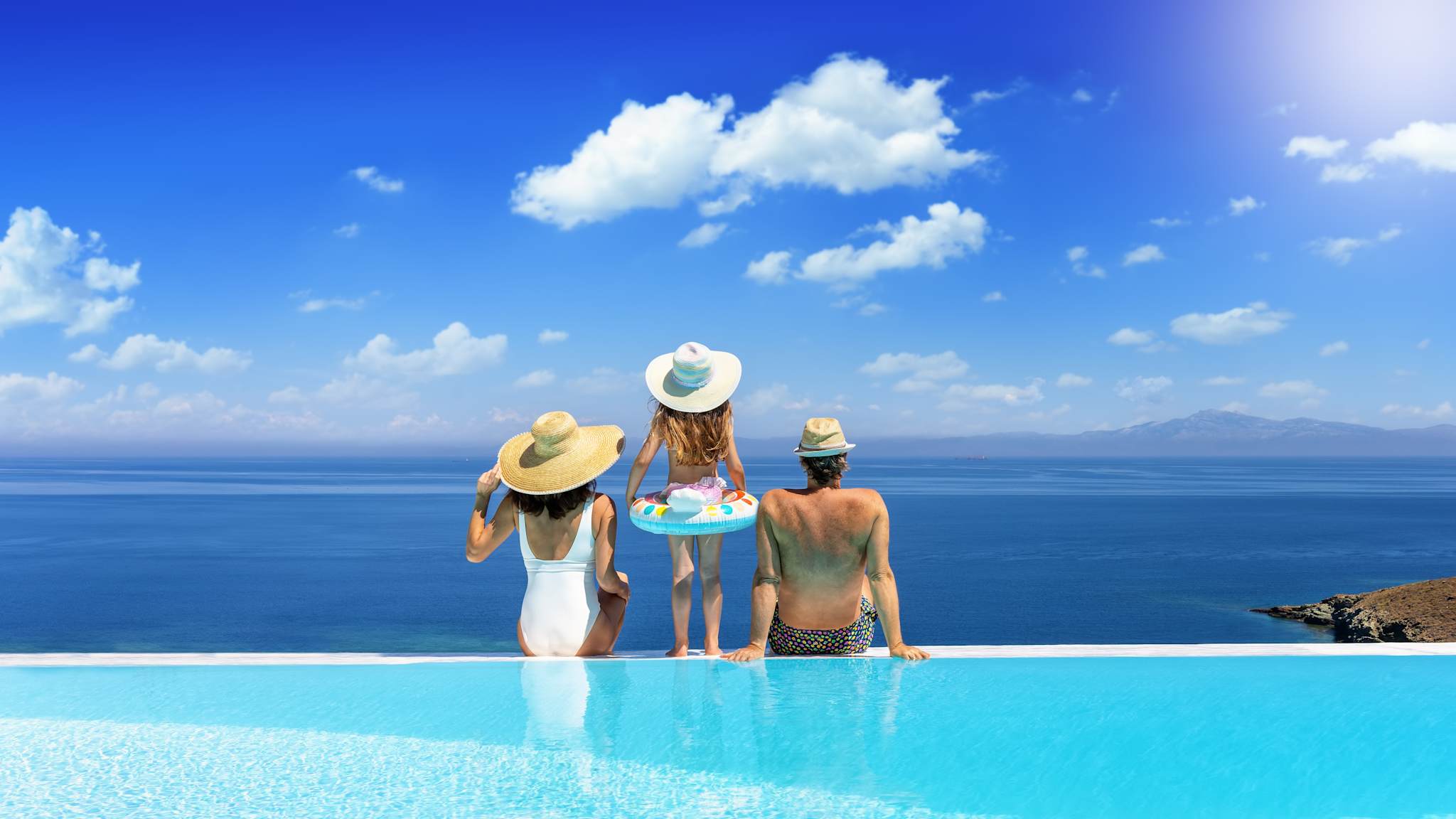 Familie sitzt am Pool mit Blick aus Meer