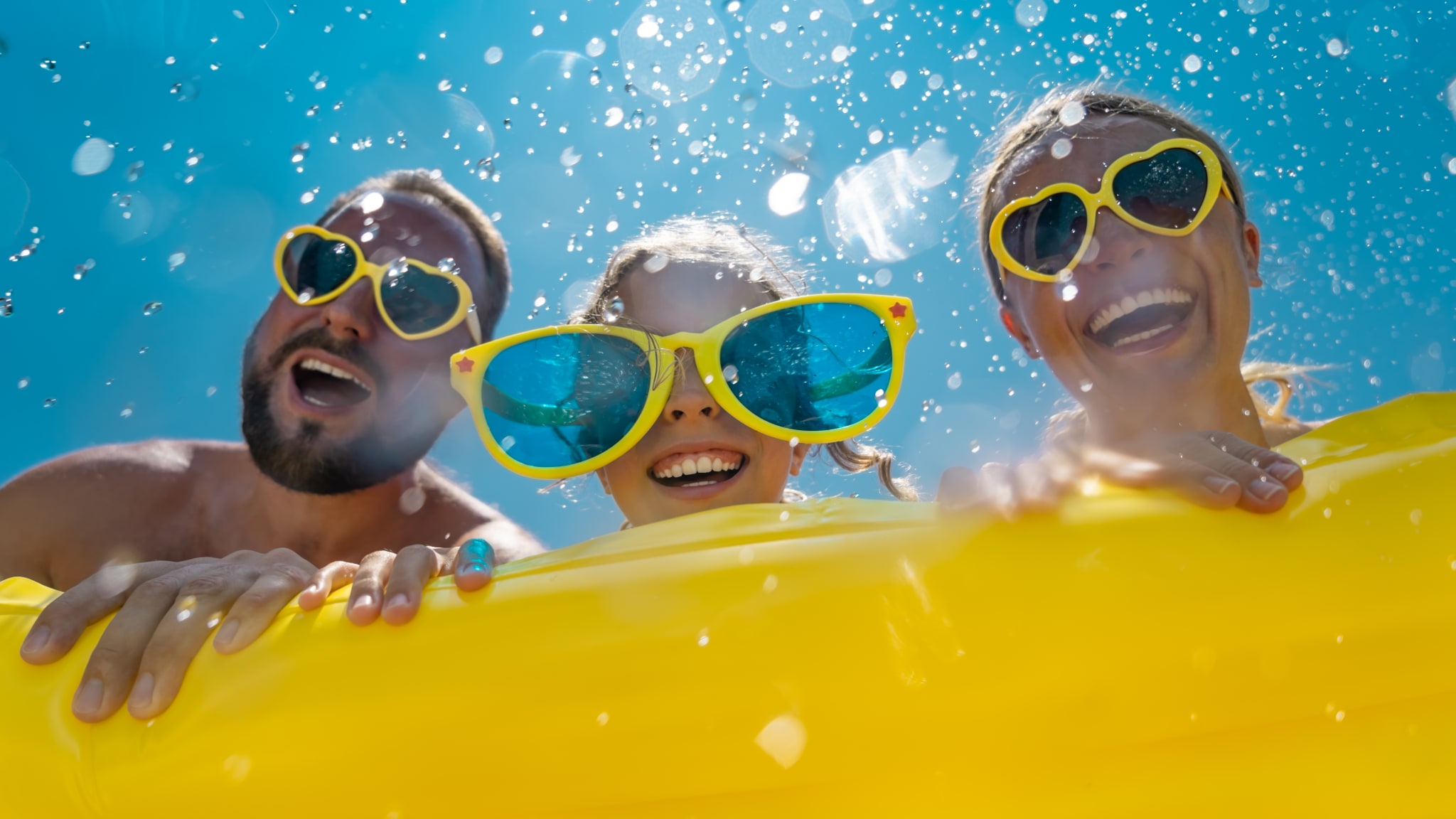Familie hat Spaß im Wasser, alle tragen gelbe Sonnenbrillen.