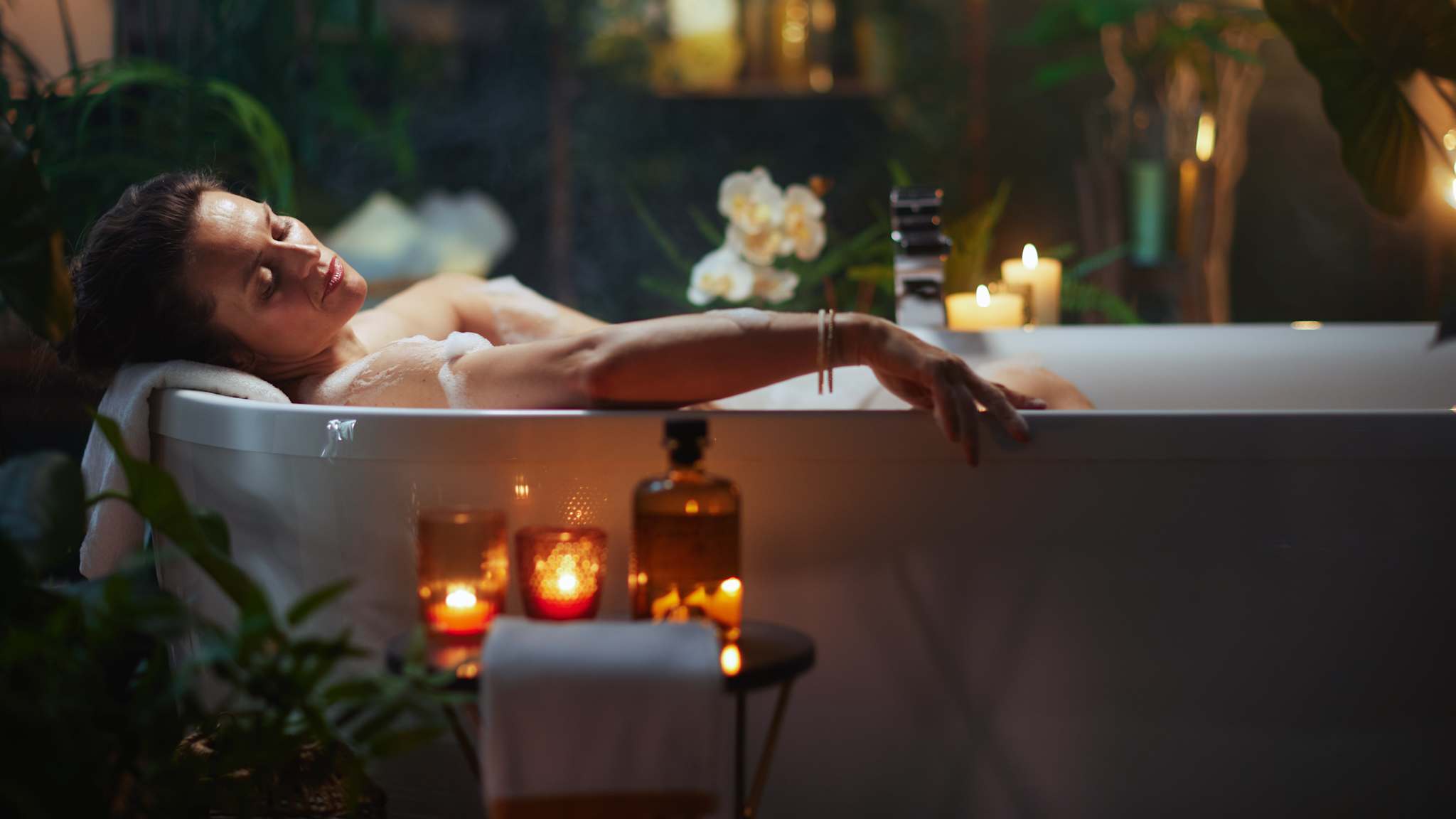 Frau liegt bei Kerzenschein in Badewanne und entspannt.
