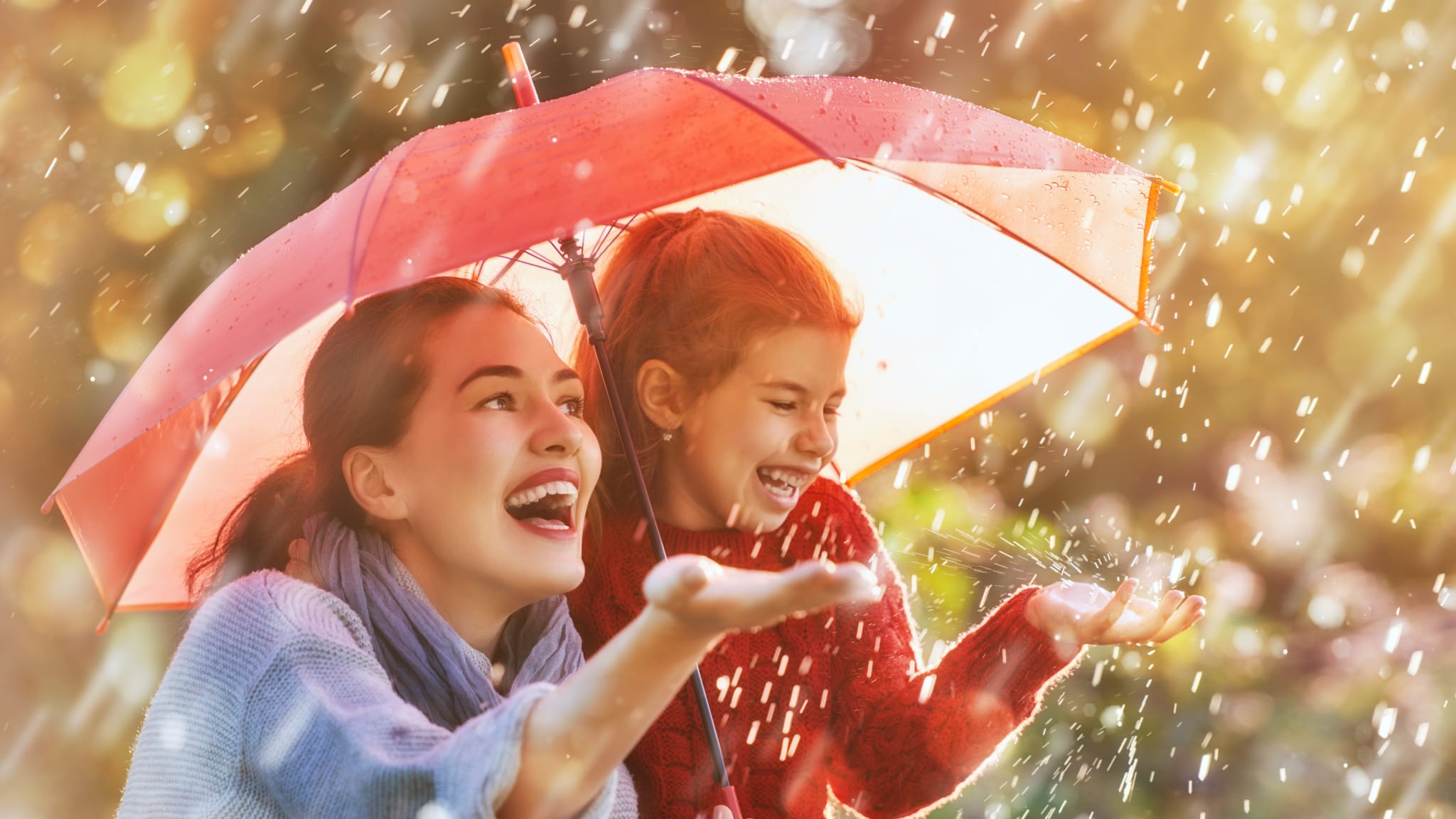 Mutter mit Kind bei Regen glücklich unter Regenschirm.