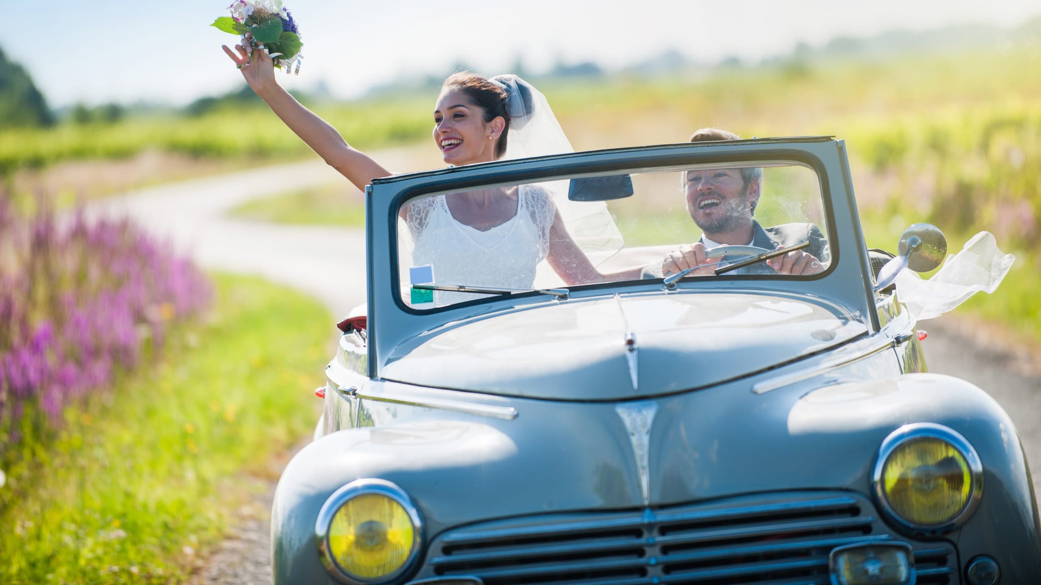 Ein Hochzeitspaar fährt mit dem Auto in die Flitterwochen.