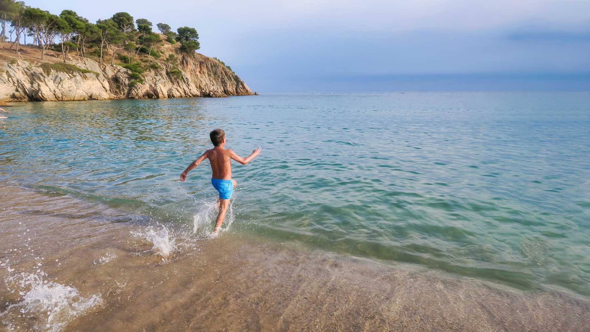 Kind läuft am Strand ins Meer an der Costa Brava, Spanien.