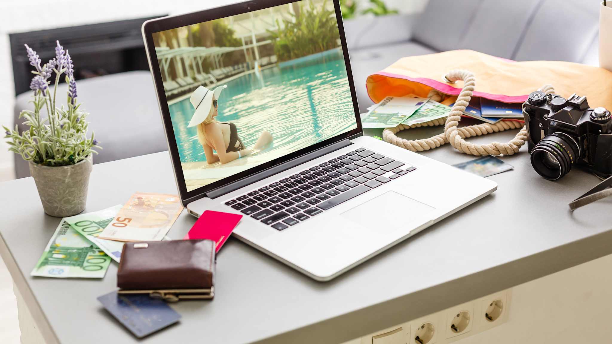 Laptop mit Urlaubsbild, Kamera, Tasche und Bargeld auf einem Tisch.