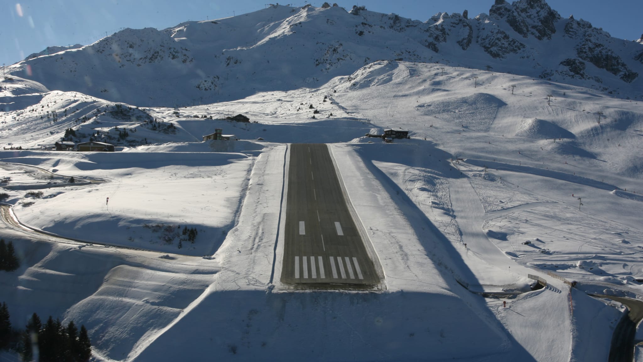 Blick von oben auf einen Runway, der auf allen Seiten von verschneiten Bergen umgeben ist.
