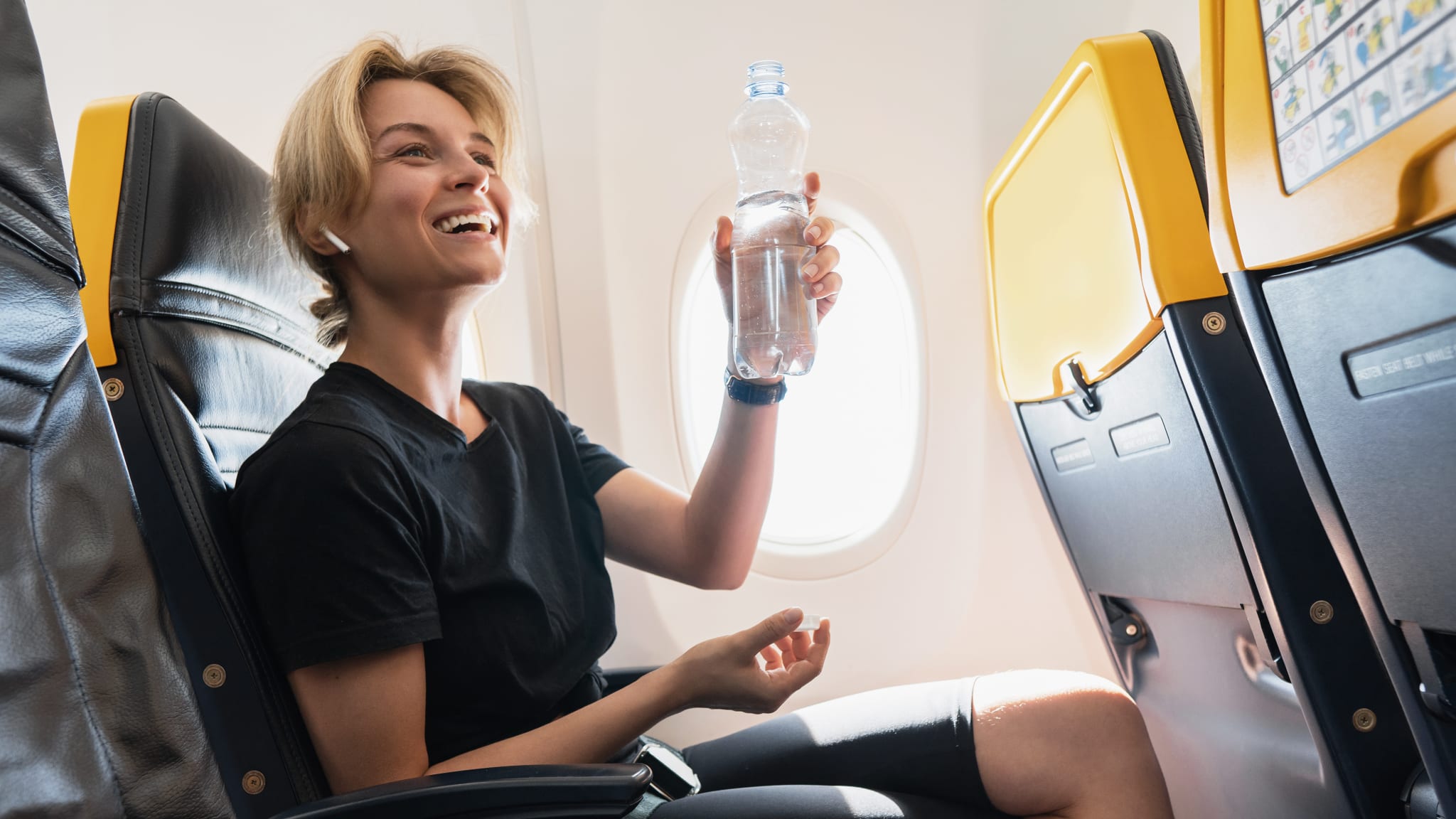 Eine Frau sitzt im Flugzeug mit einer Flasche Wasser in der Hand