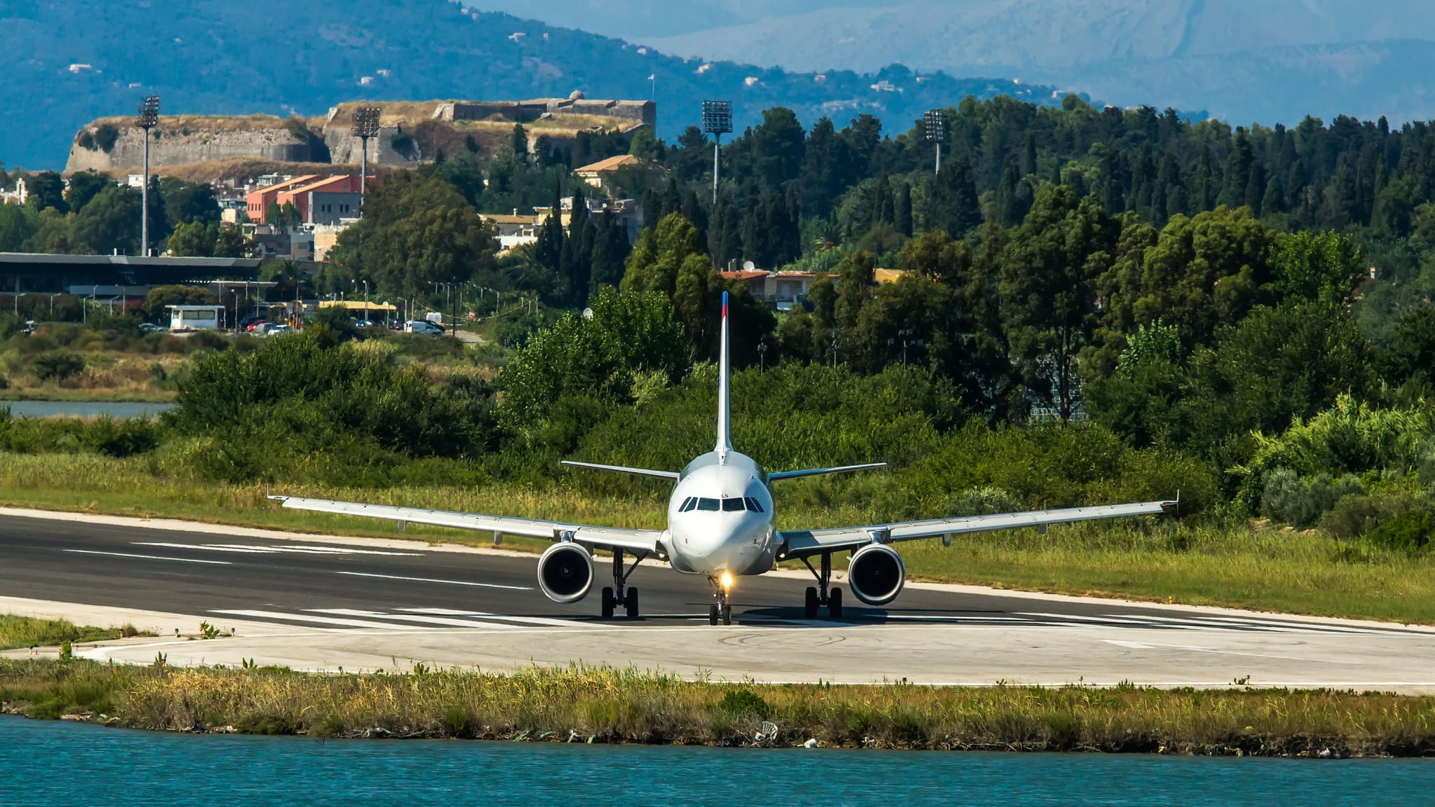 Ein Flugzeug auf der Landebahn. Im Vordergrund ist Meer, im Hintergrund sind Berge zu sehen.