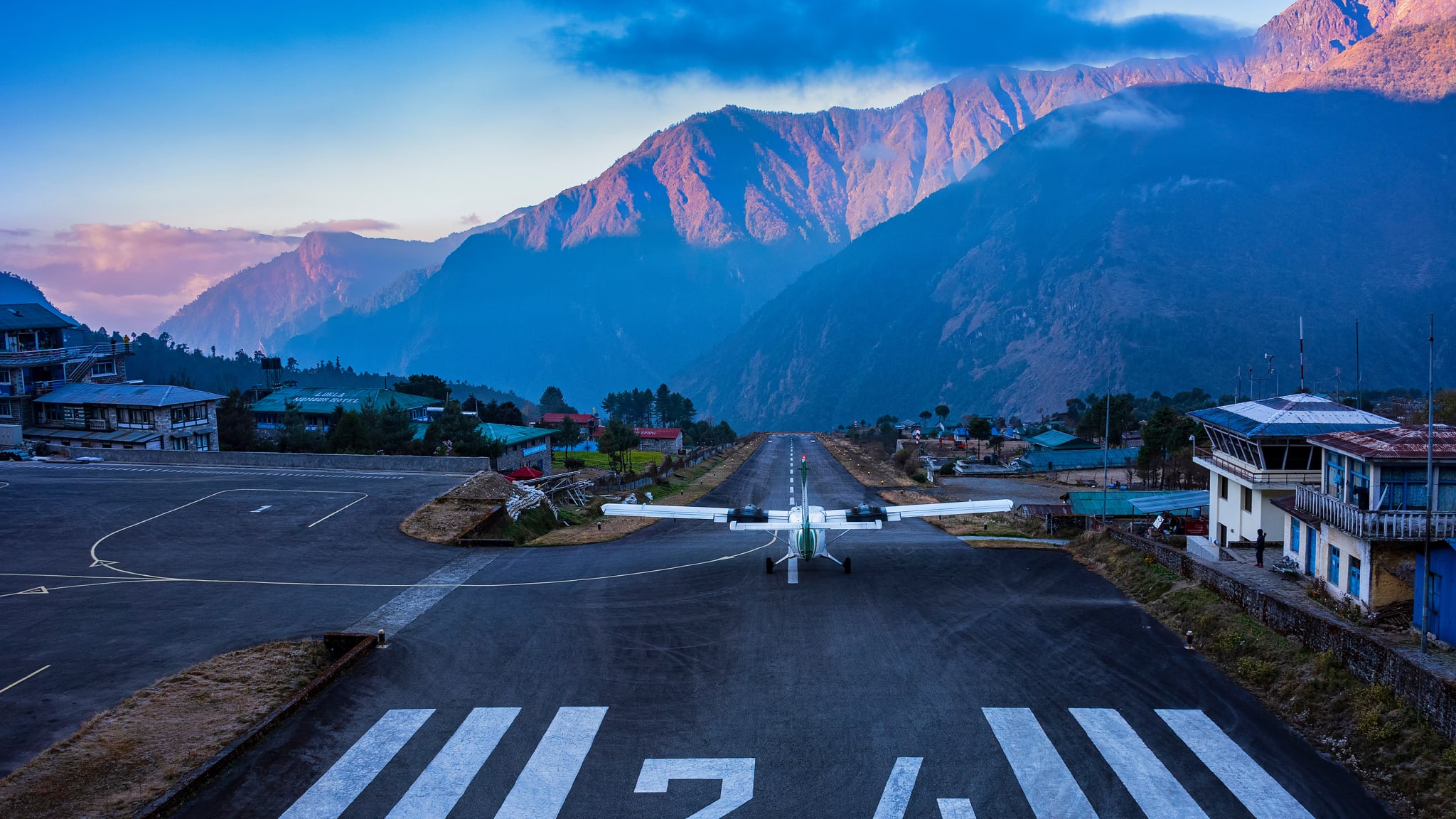 Ein kleines Flugzeug ist bereit abzuheben von einer Landebahn. Im Hintergrund sind große Bergketten.