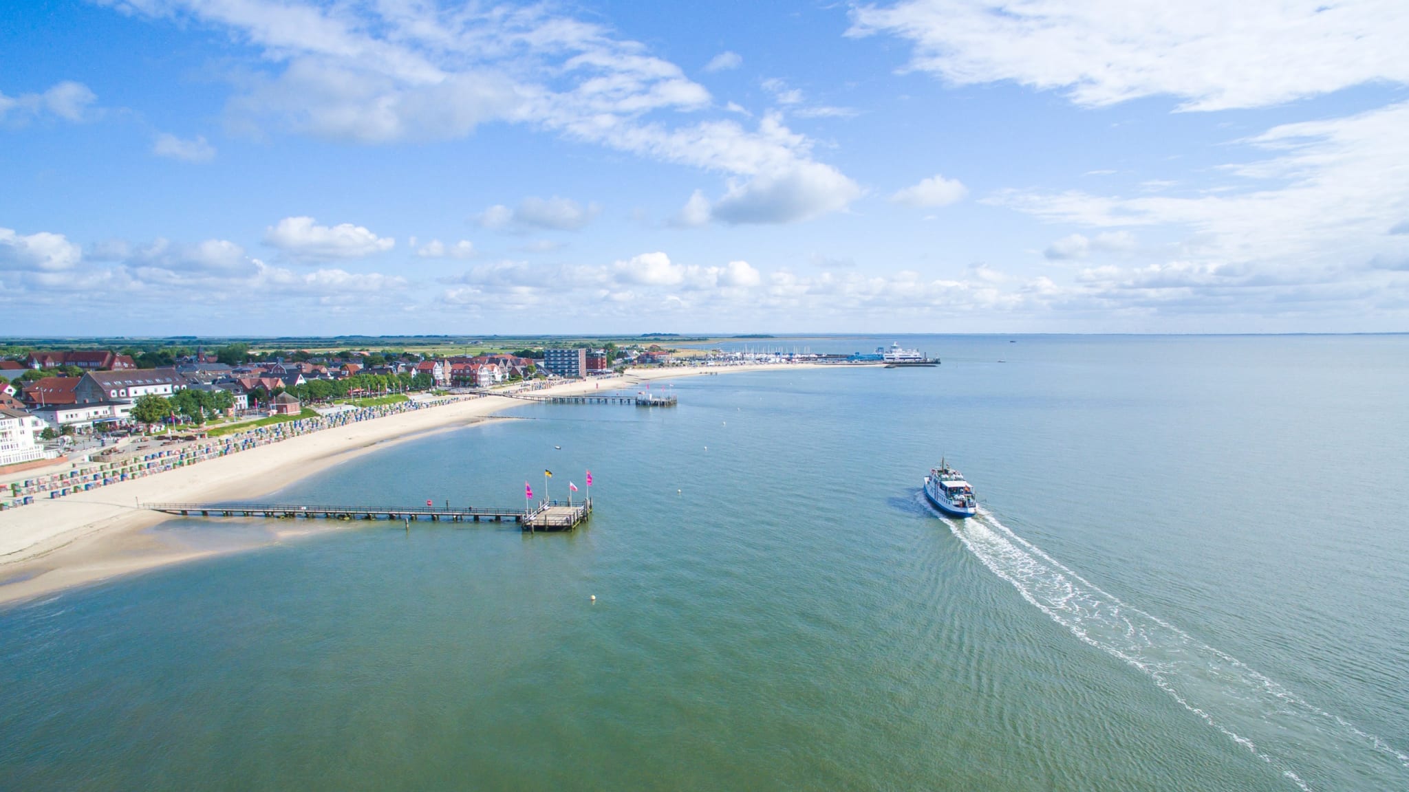 Blick von oben auf einen Strand mit mehreren Stegen und einem Boot