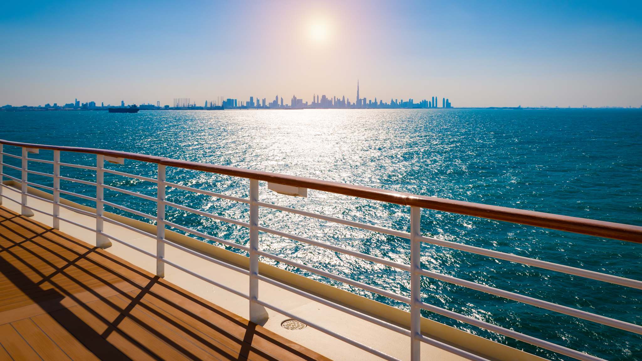 Blick über die Reeling eine Kreuzfahrtschiffes auf die sonnenbeschienene Skyline von Dubai