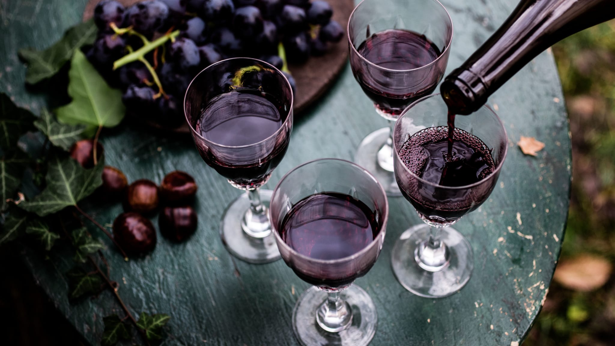 Ein Teller mit roten Trauben und vier Gläsern, in die gerade Wein gefüllt wird