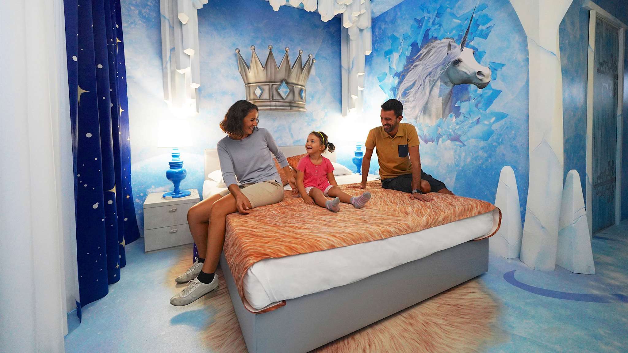 Mutter, Vater und Tochter in einem Hotelzimmer mit Einhornmotiv auf der Tapete