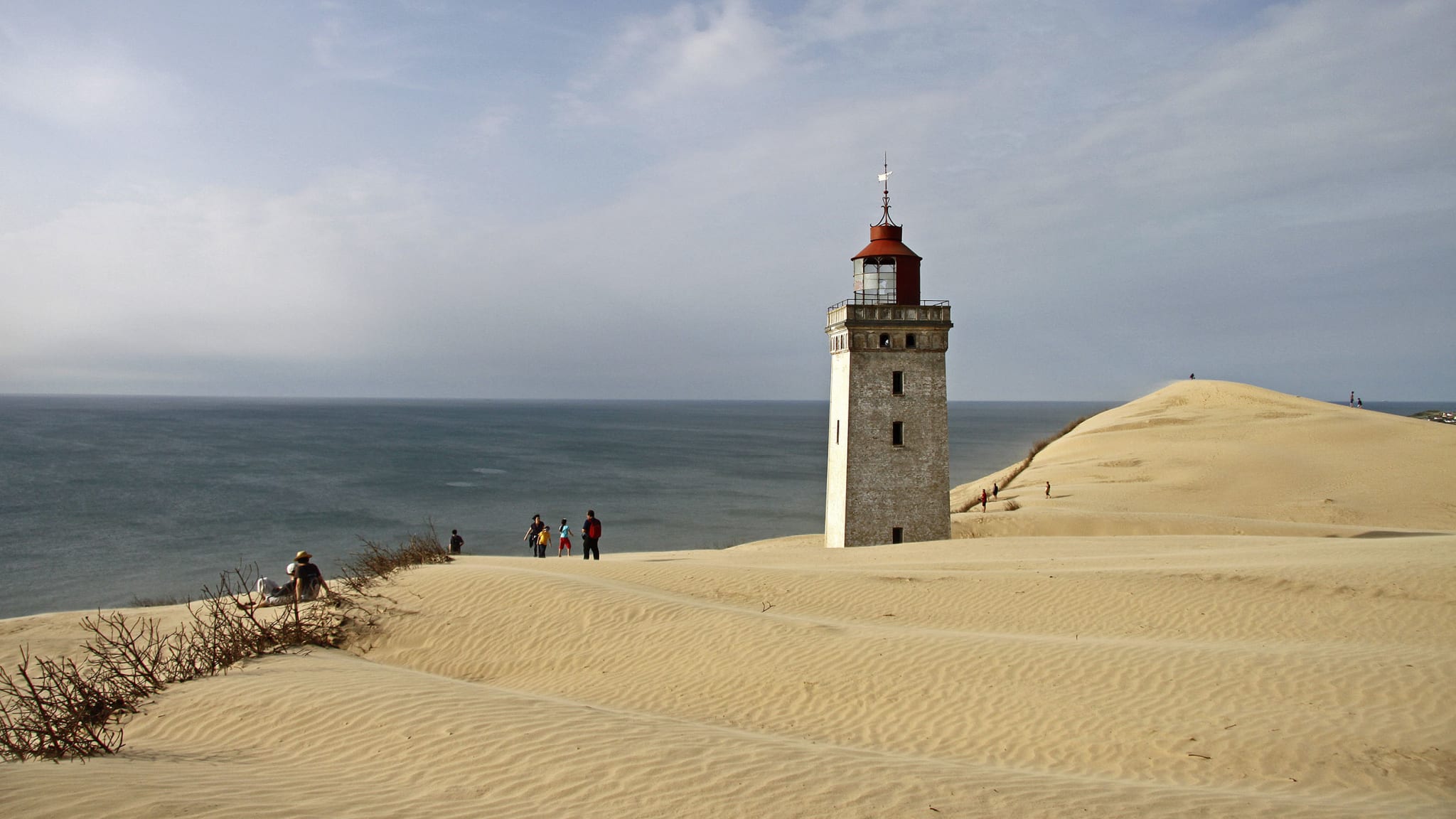 Ein Leuchtturm steht in einer großen Düne. Dahinter ist das Meer.