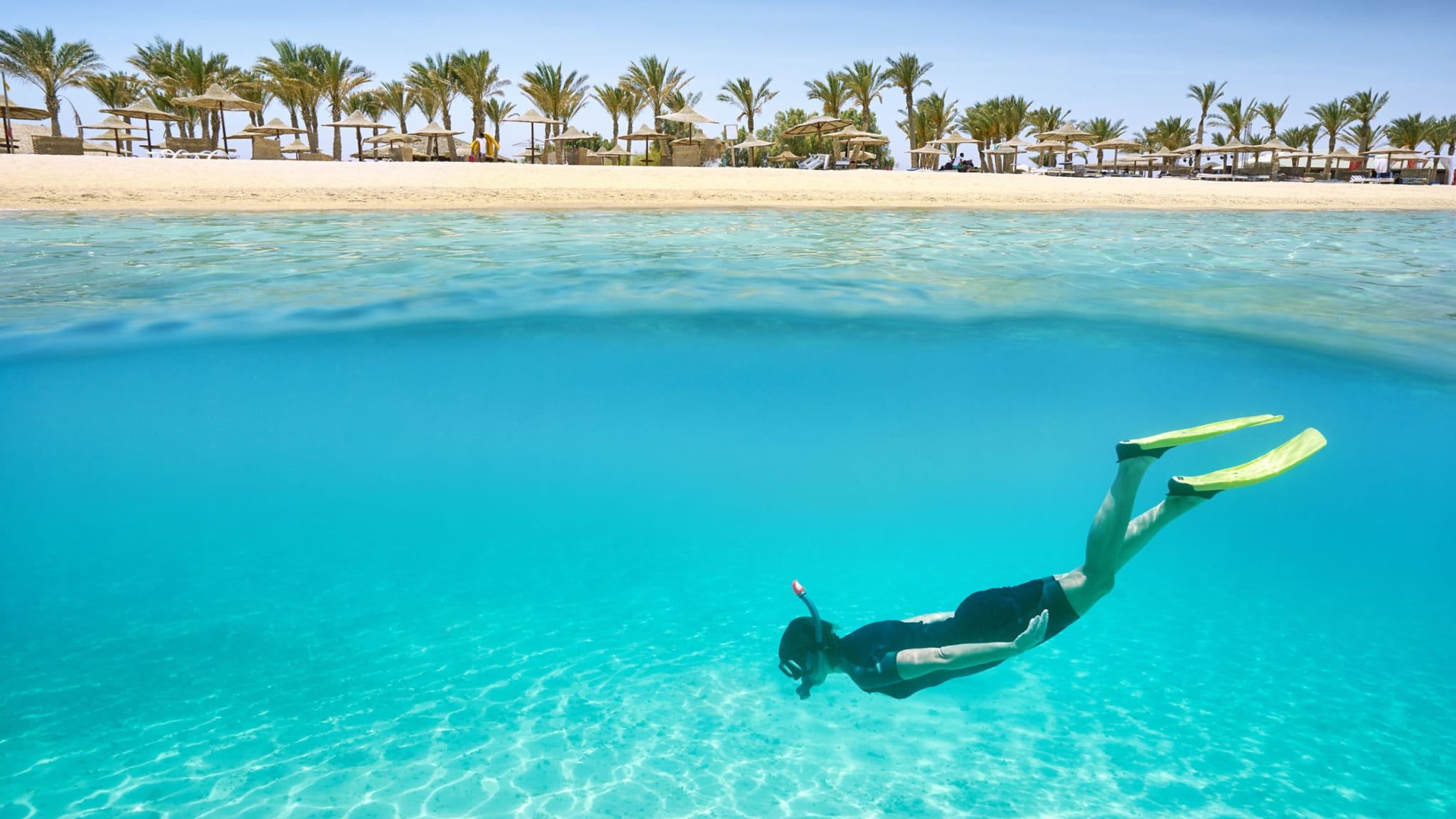 Taucherin in Marsa Alam unter Wasser mit Strand im Hintergrund