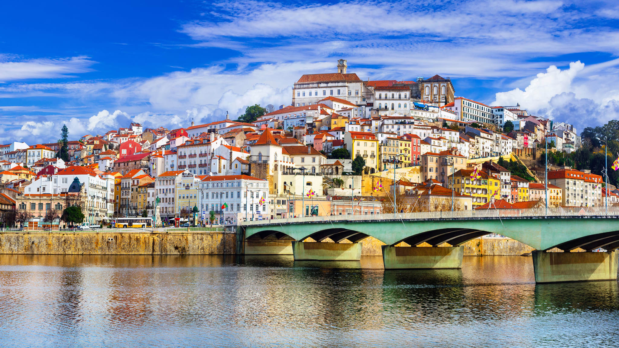 Fluß mit grüner Brücke, dahinter aufragend die Stadt Coimbra