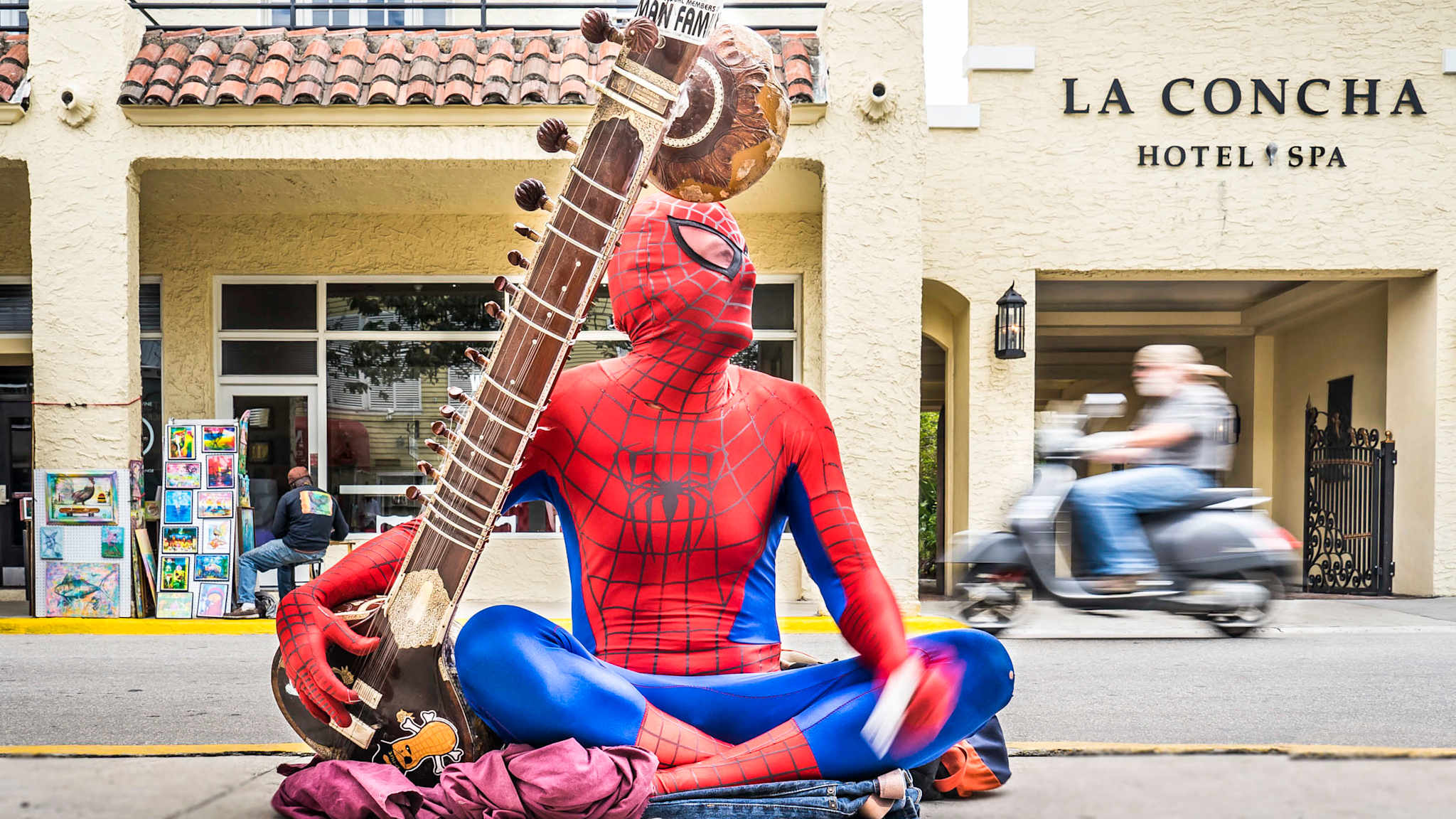 Straßenmusiker mit Sitar und Spiderman-Kostüm und Mann auf Roller in der Duval Street im Zentrum von Key Wes