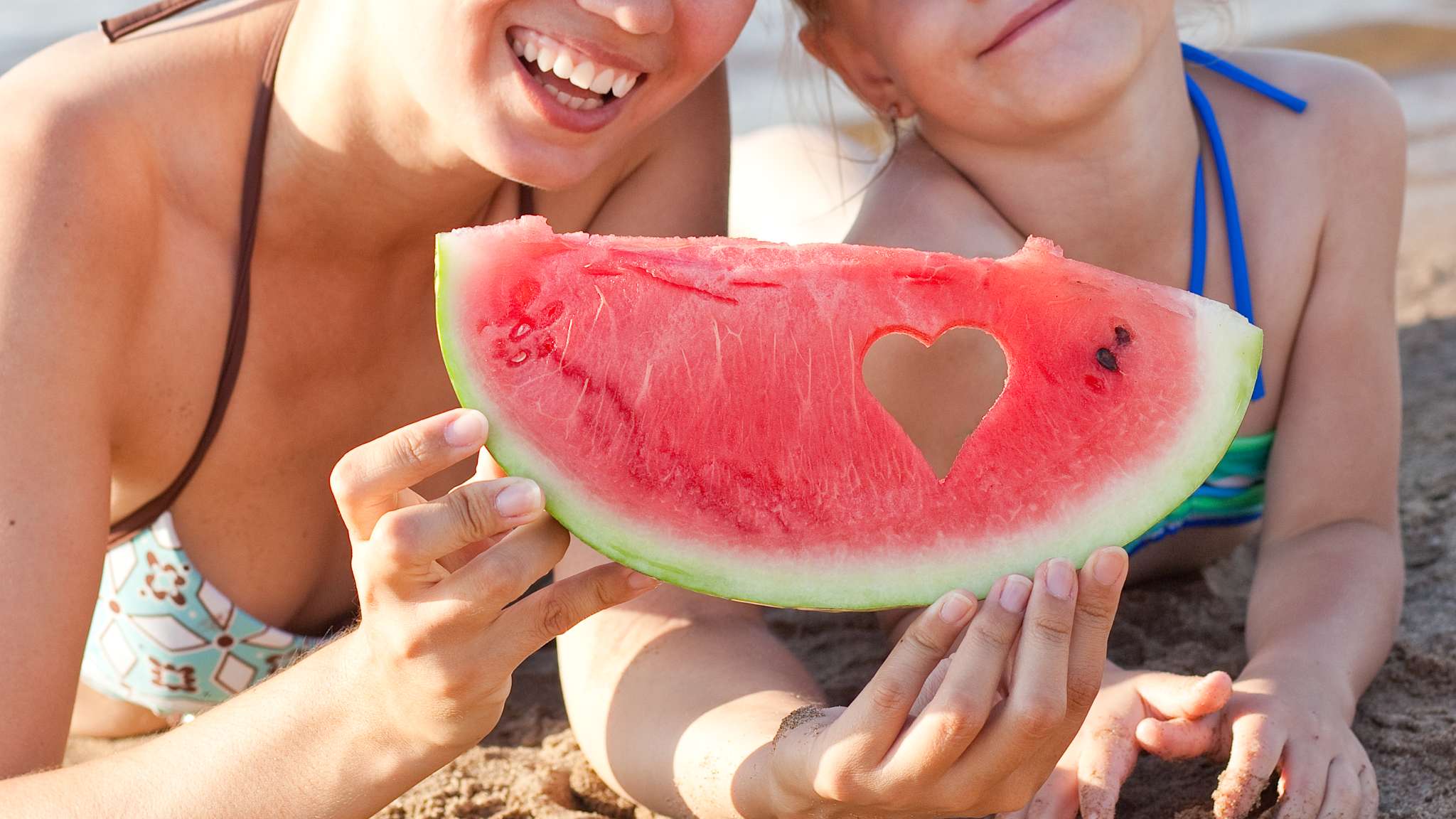 Mutter mit Tochter am Strand im Sommerurlaub mit einem Stück Wassermelone.