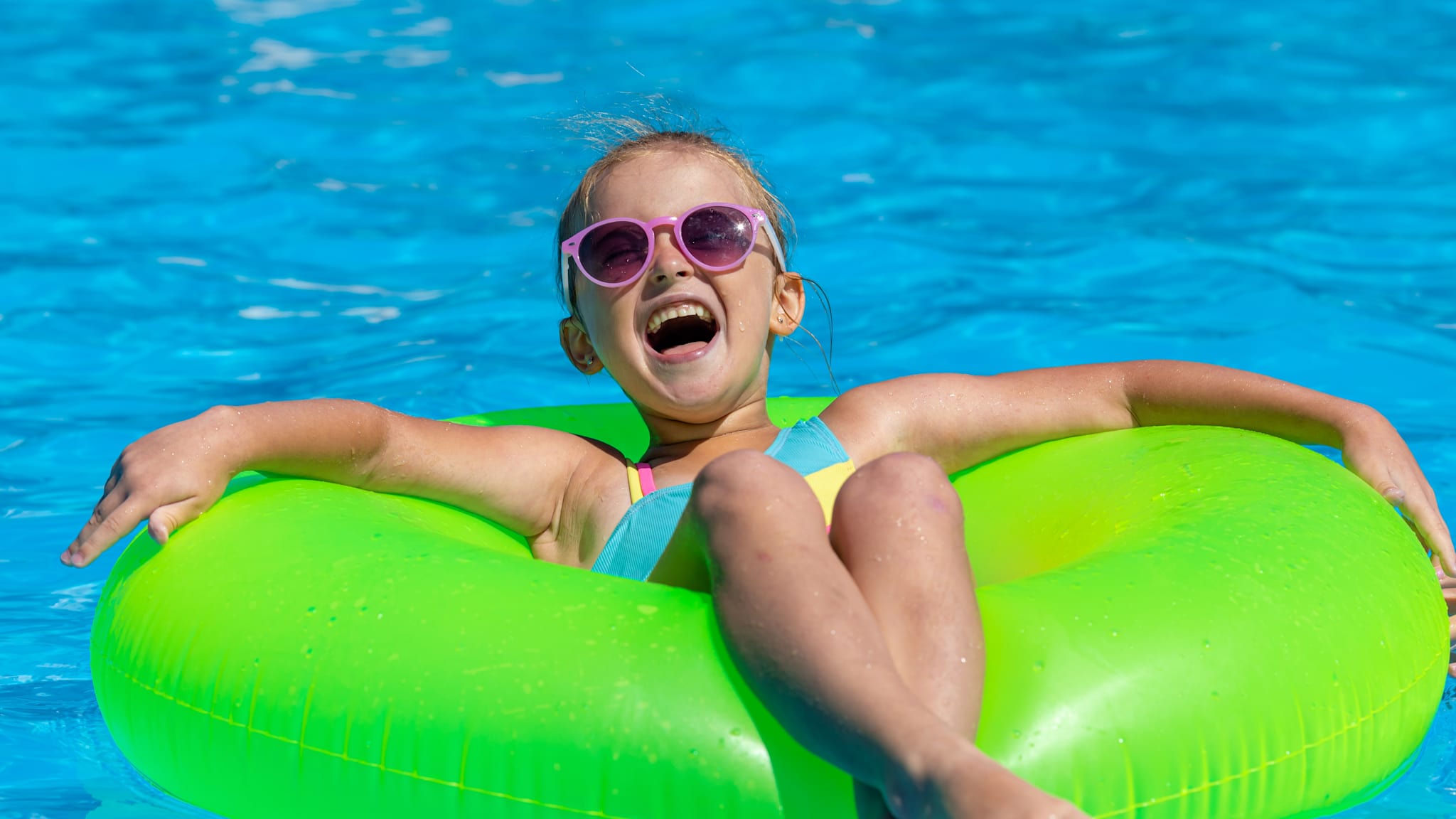 Kleines Mädchen lacht und hat Spaß auf einem Schwimmring im Pool.