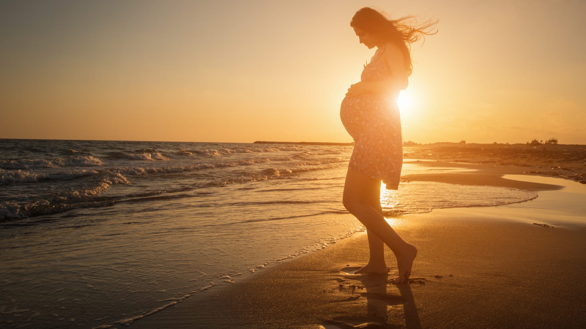 Frau mit Babybauch am Strand.