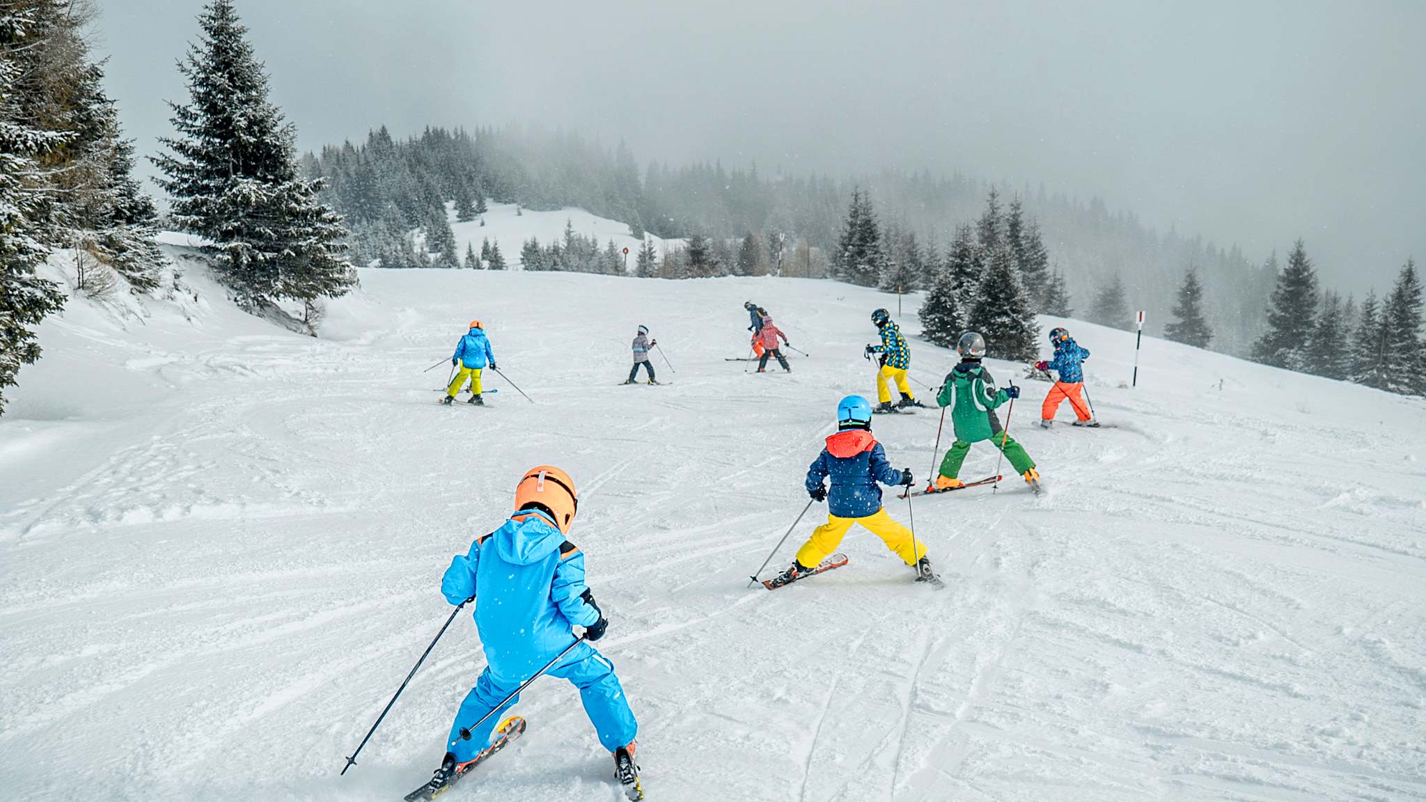 Ein Skischul-Kurs fährt in einer Gruppe schneebeckte Pisten runter.