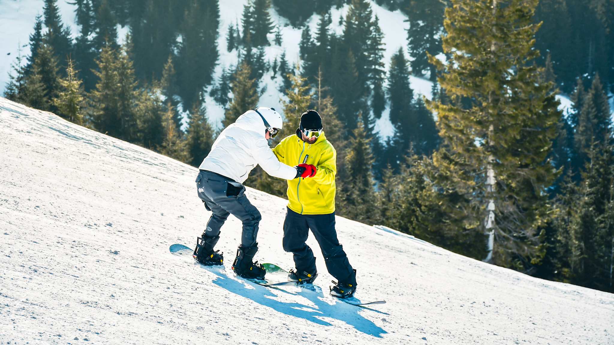 Ein Mann lernt das Snowboarden mit einem Lehrer auf der schneebedeckten Piste.