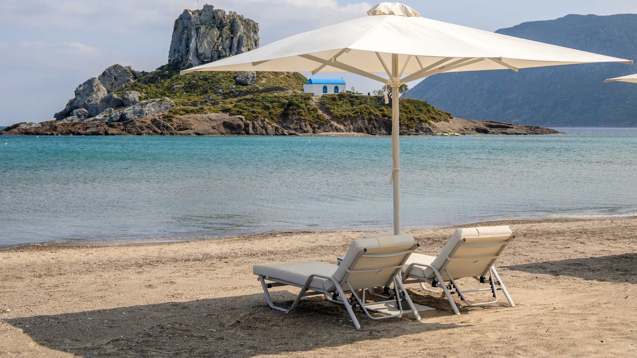 Strand Agios Stefanos mit zwei Liegen und Sonnenschirm auf Kos, Griechenland.