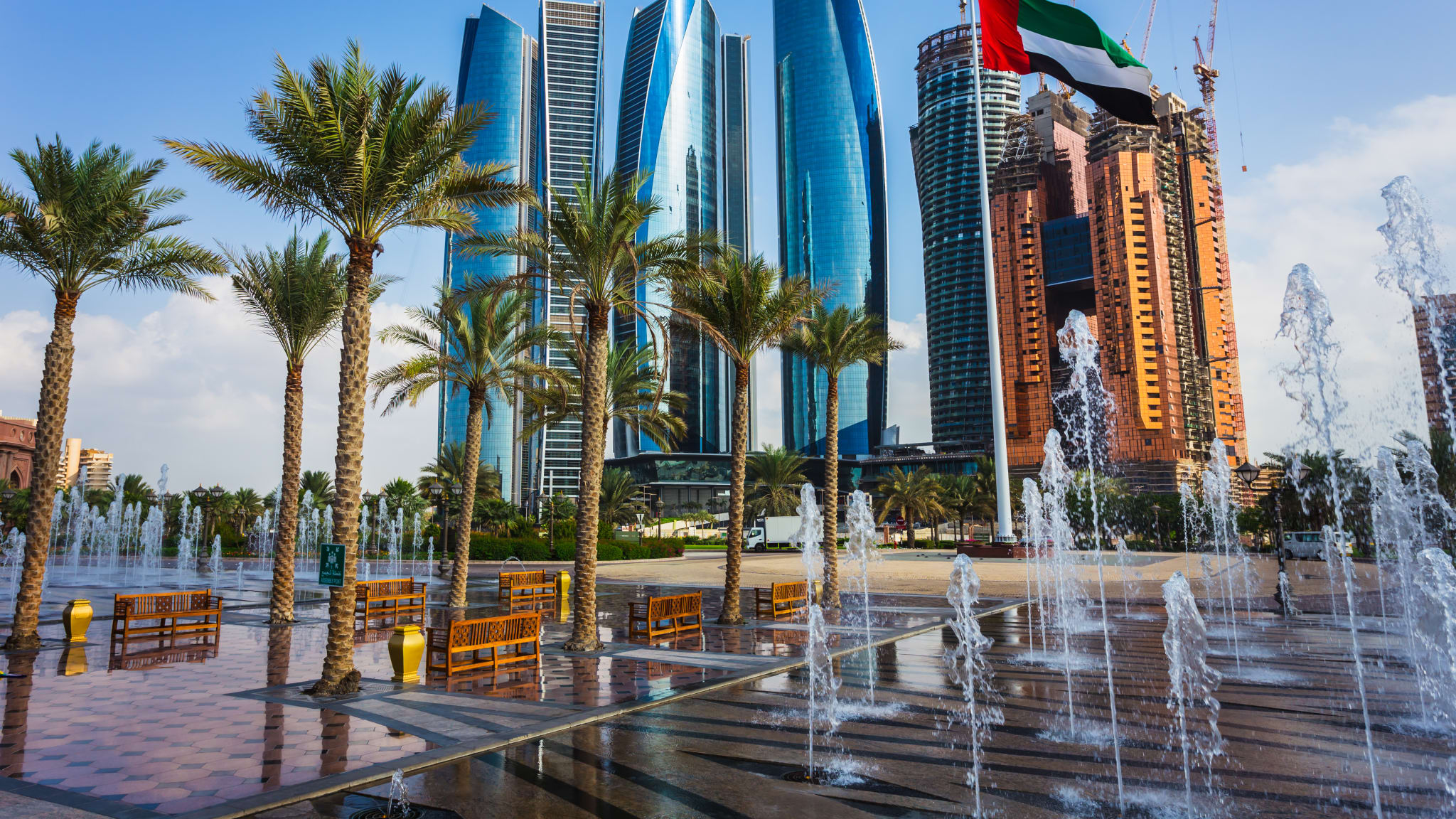 Palmen und Springbrunnen auf Platz vor Wolkenkratzer in Abu Dhabi, VAE.