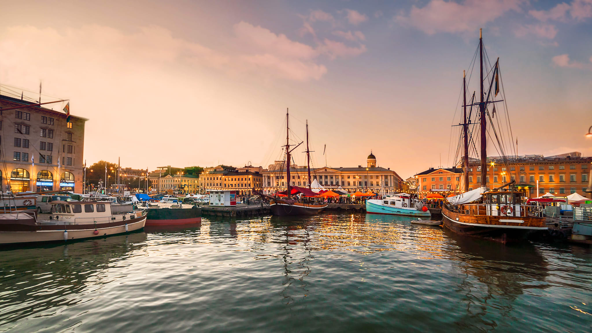 Ein Hafen bei Sonnenuntergang. Mehrere Boote liegen im ruhigen Wasser, die Promenade ist mit Lichterketten dekoriert.