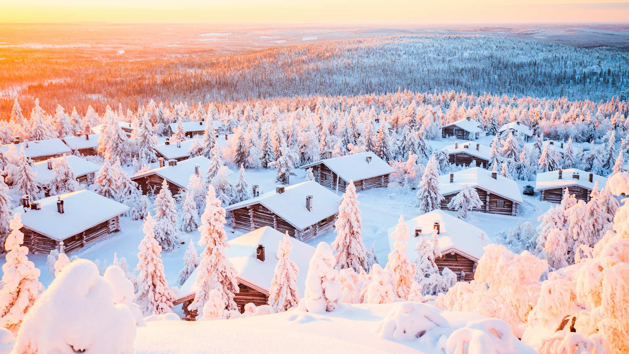 Atemberaubender Sonnenuntergang über Holzhütten und schneebedeckten Bäumen in Finnisch-Lappland ©Shutterstock | TravelPhotoBloggers