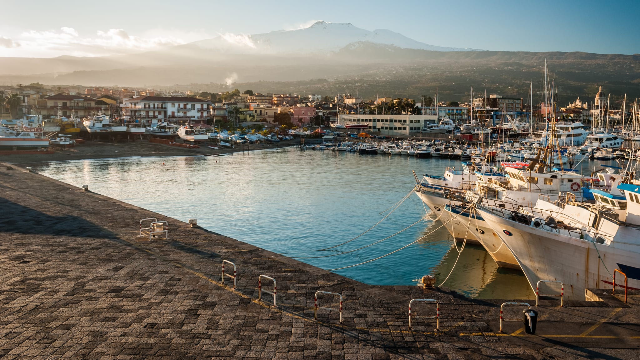 The harbor of Riposto during the sunset; snowy volcano Etna in the background