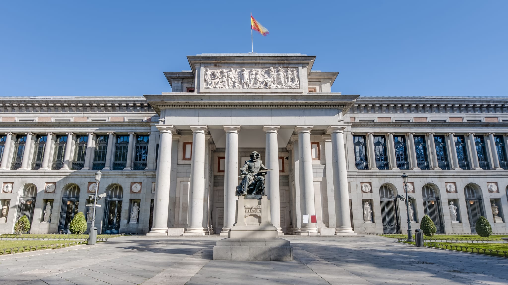 Das Museo Nacional del Prado in Madrid ist ein Gebäude mit vielen Säulen. Vor dem Eingang steht eine Statue.