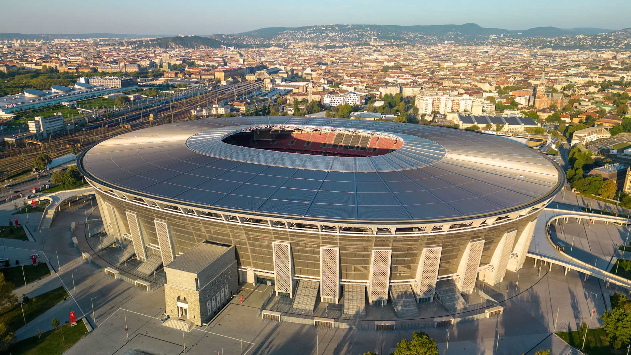 Luftaufnahme des Stadions der Puskas Arena in Budapest mit Skyline und Zuglinien im Hintergrund©Shutterstock | Wirestock Creators