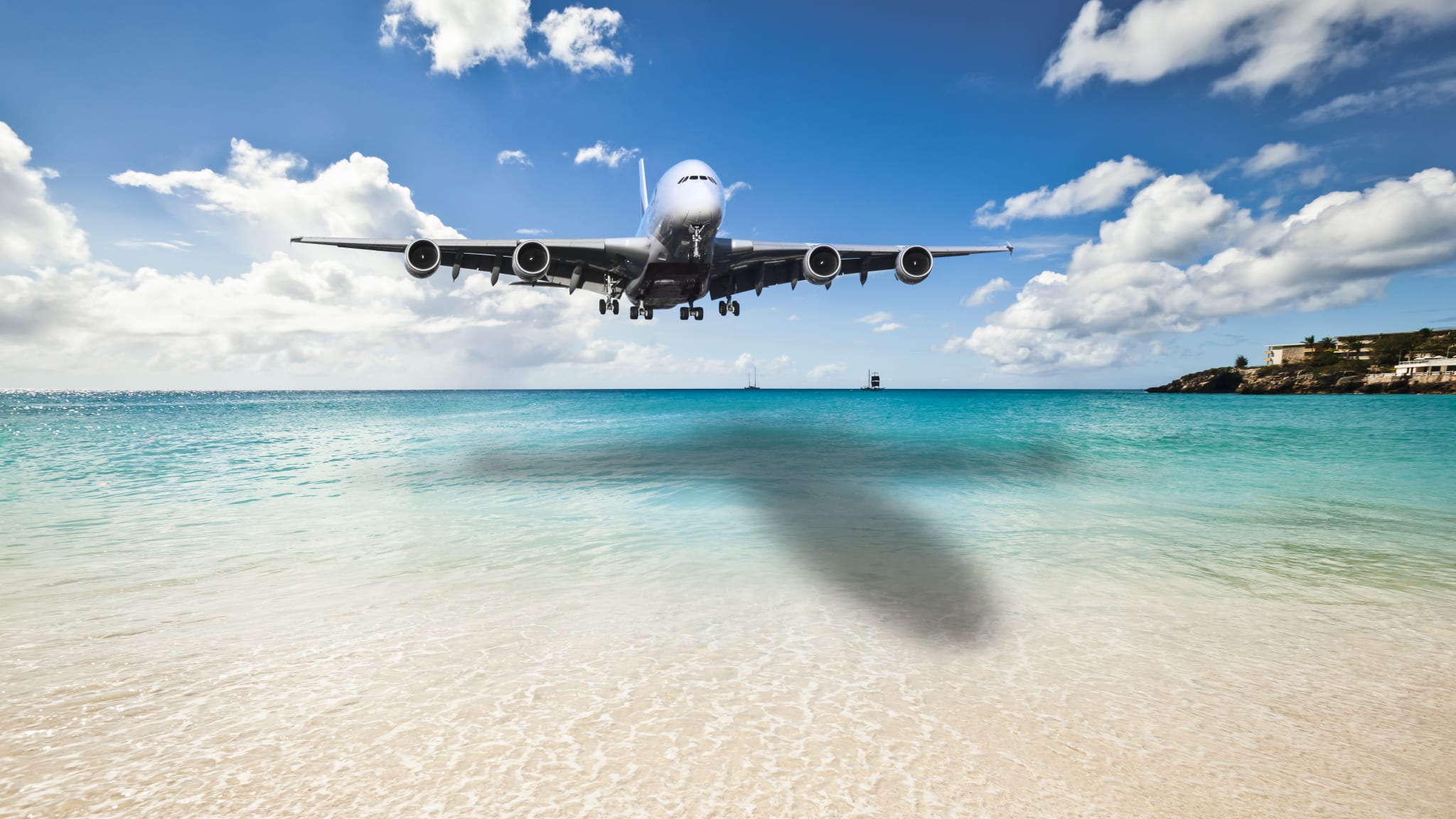 Ein Flugzeug ist im Landeanflug über einem Strand mit ruhigem Wasser.