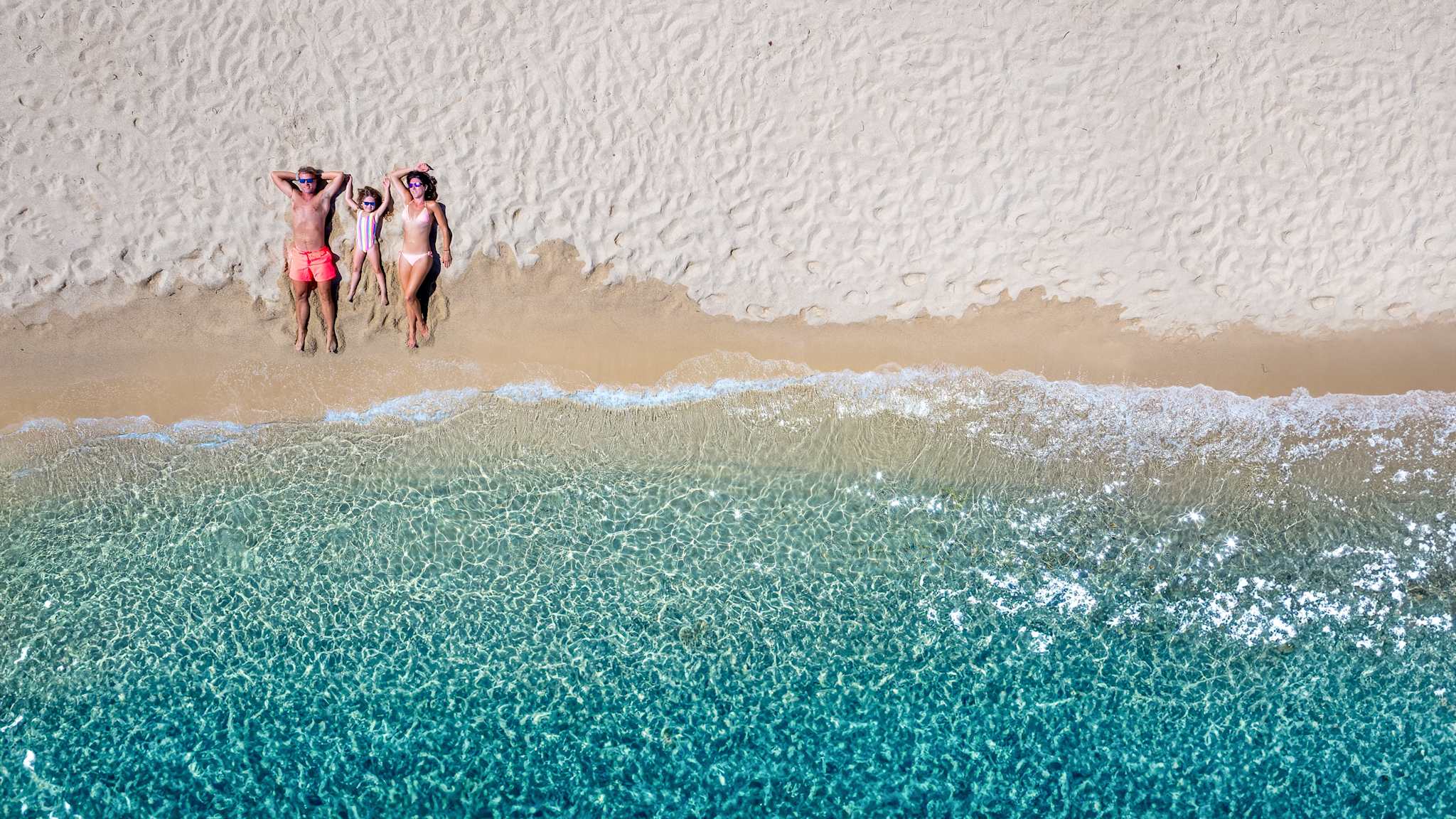 Dreiköpfige Familie liegt am Strand und genießt die Sonne im Familienurlaub © Shutterstock