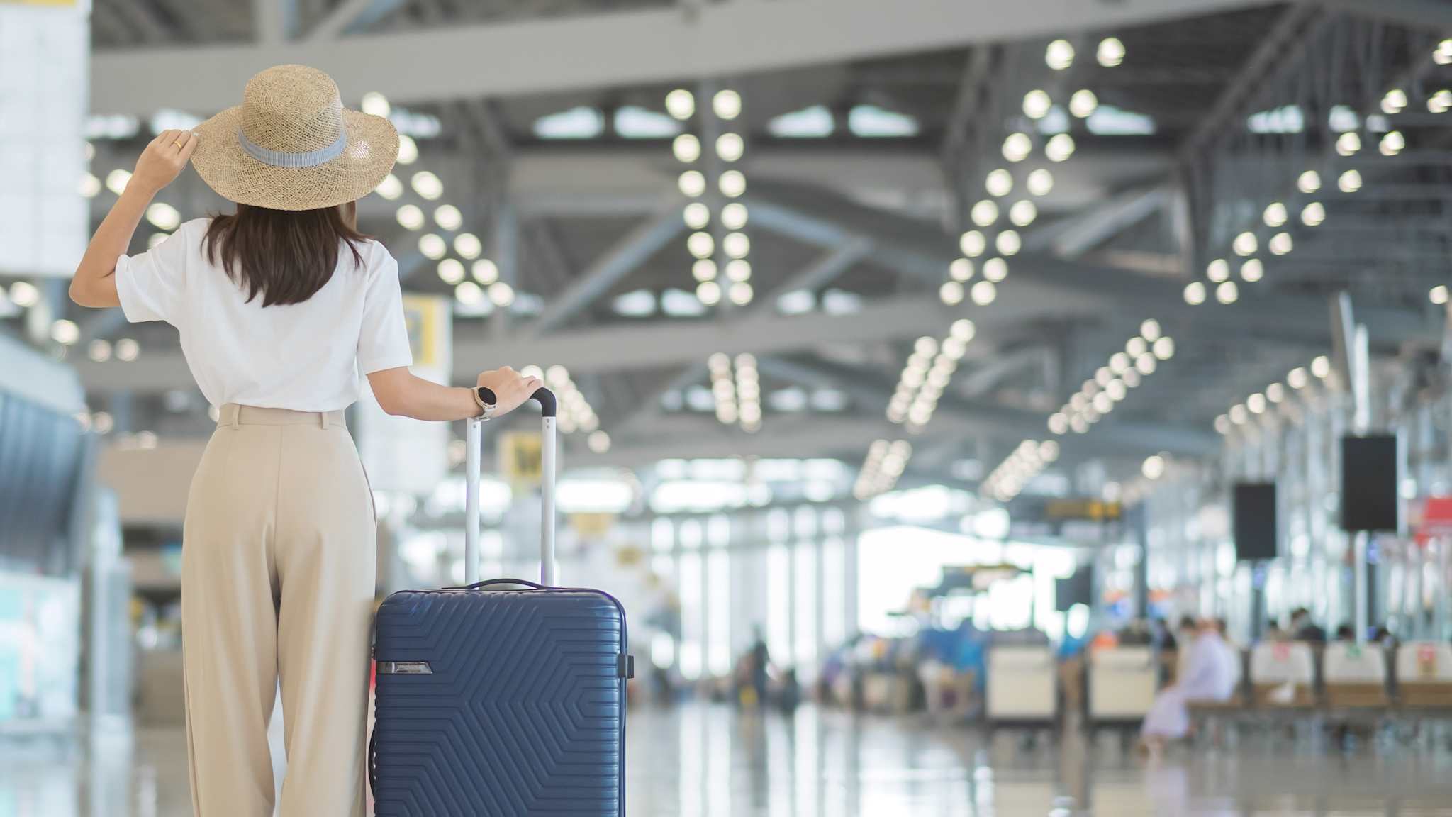 Frau steht mit Sonnenhut am Flughafen © Shutterstock