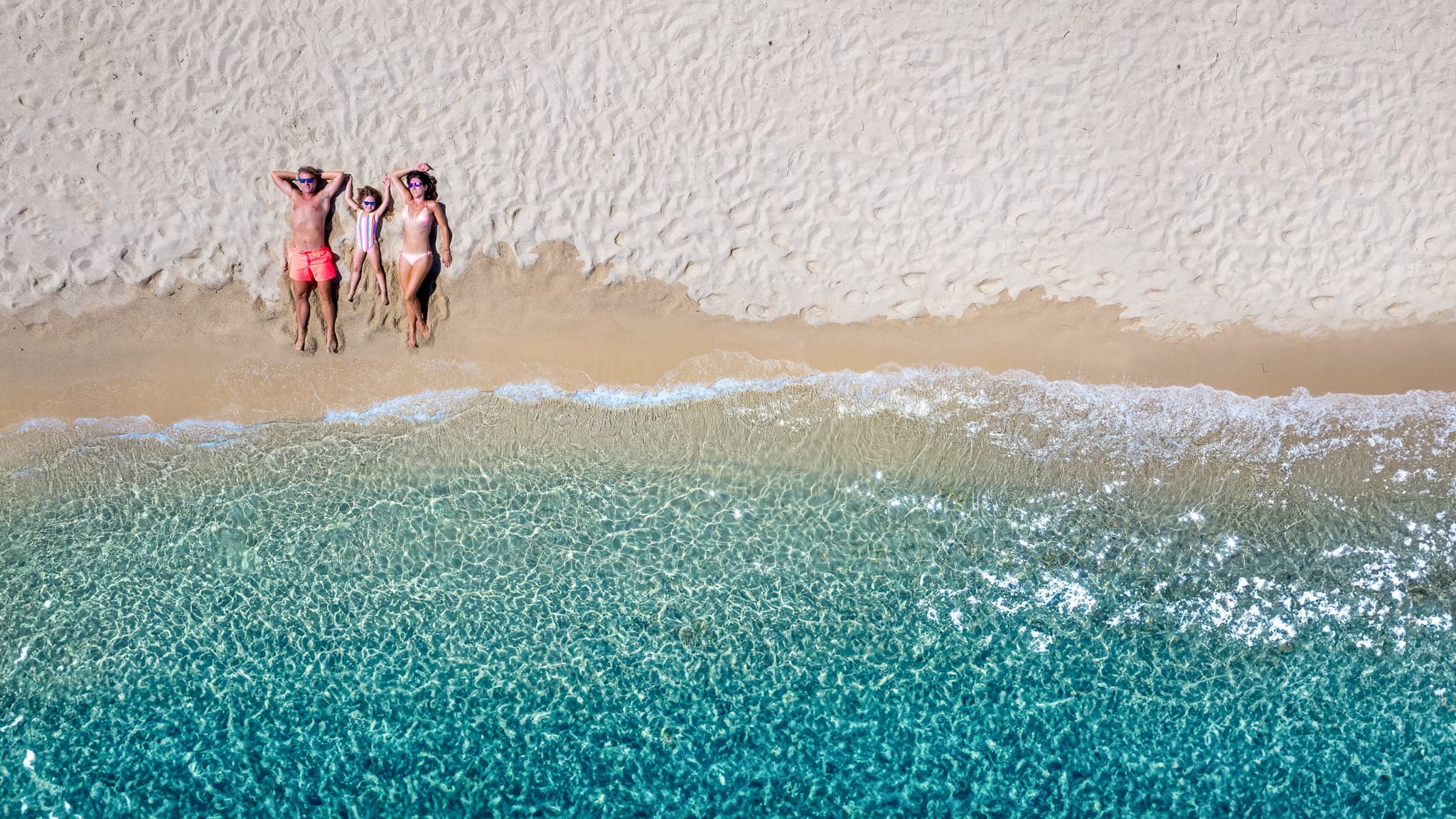 Vater, Mutter und Kind liegen an einem Strand am Meer.