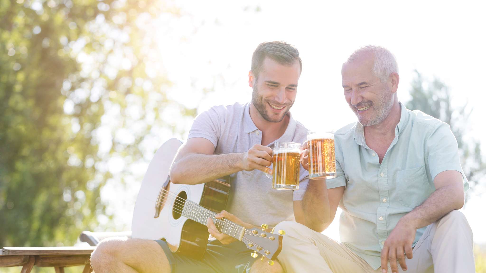 Vater und Sohn sitzen zusammen im Garten und stoßen mit einem Bier an