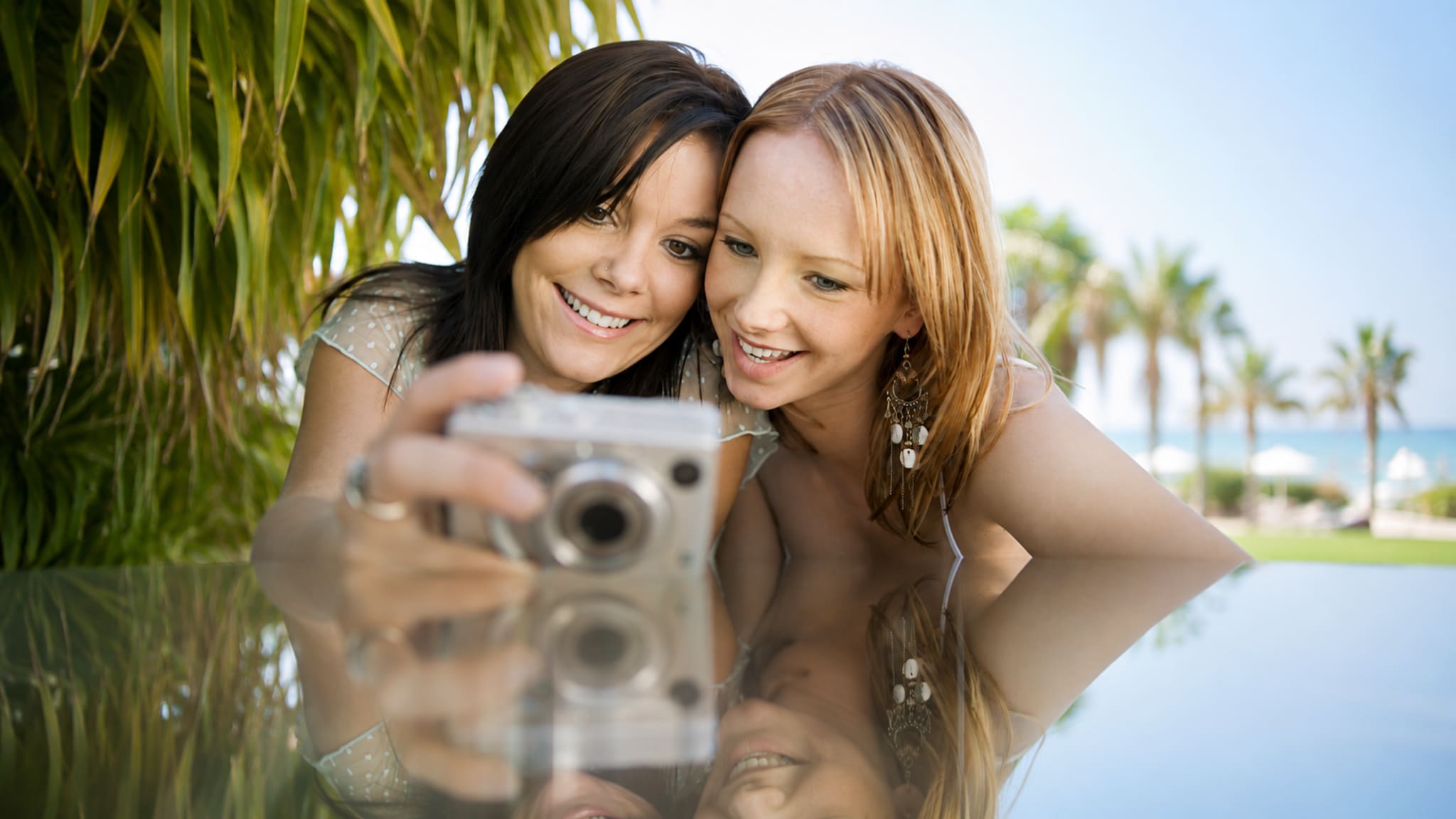 Zwei Frauen fotografieren sich mit einer Digitalkamera im Urlaub.