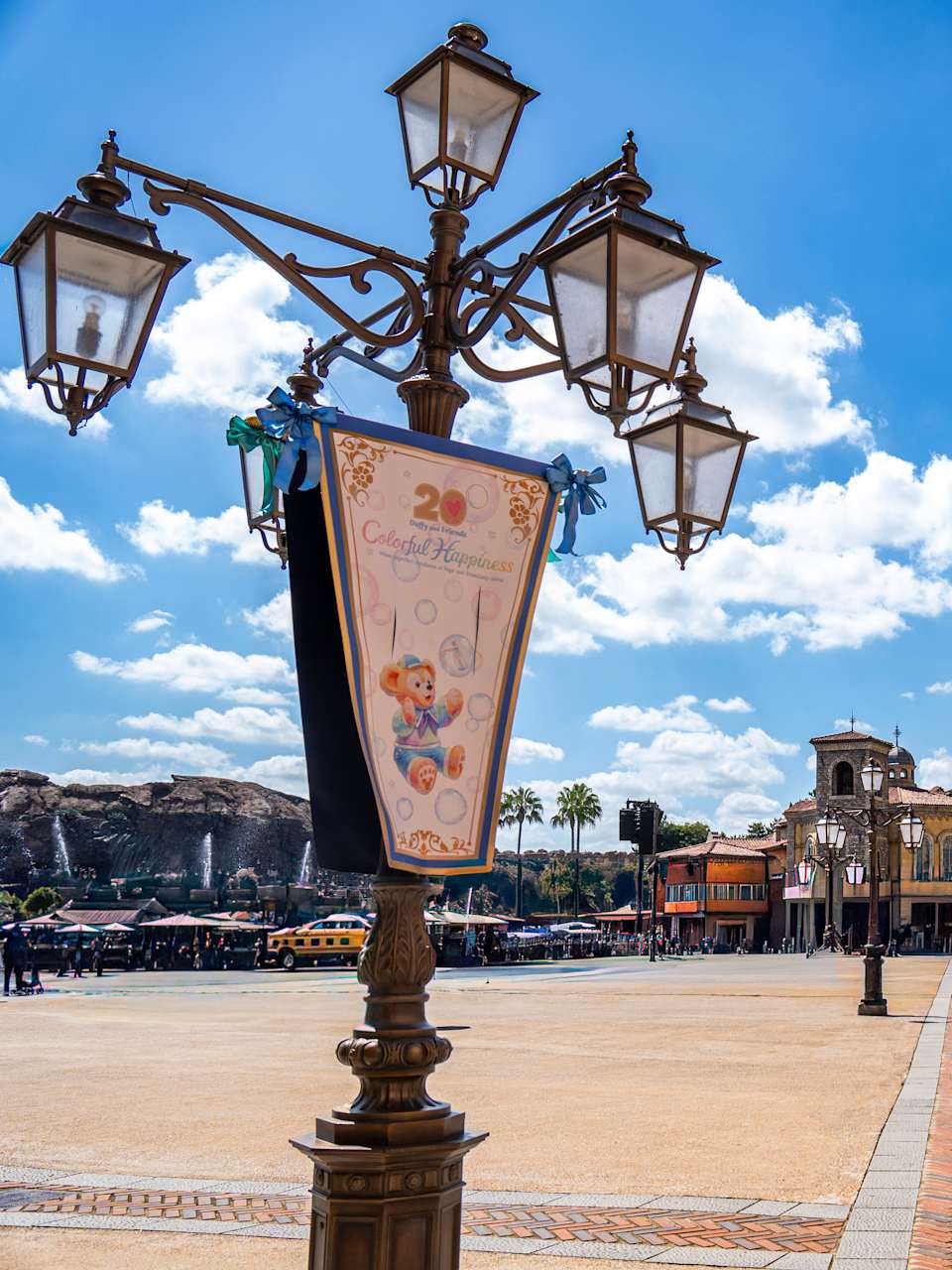 Ein Platz mit bunten, ästhetischen Häusern am Rand, einer verschnörkelten Laterne im Vordergrund und im Hintergrund Berge mit kleinen Wasserfällen im DisneySea bei Tokyo, Japan.